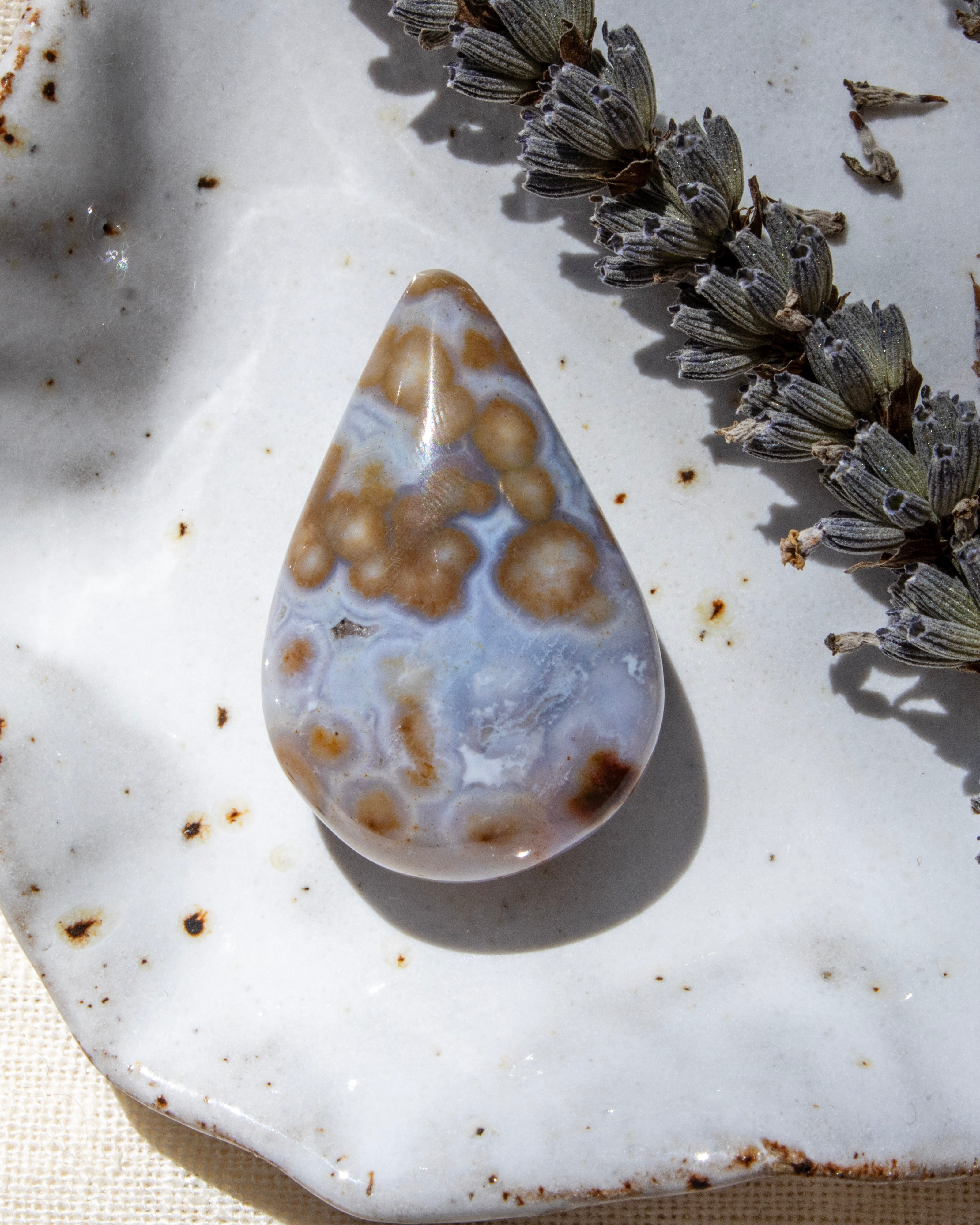 Teardrop-shaped agate stone on a textured surface with dried lavender.
