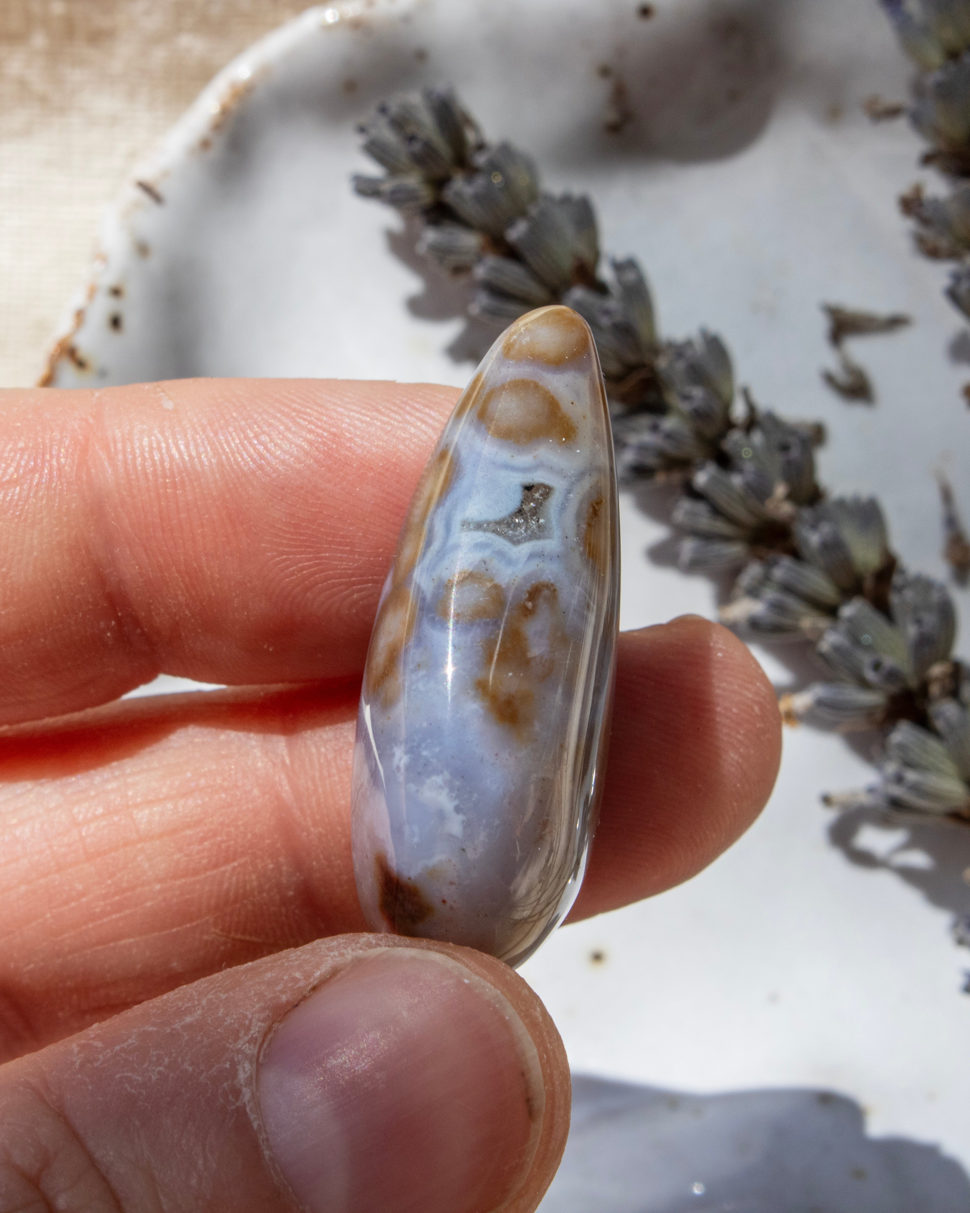 Teardrop-shaped agate stone being held with dried lavender in the background.