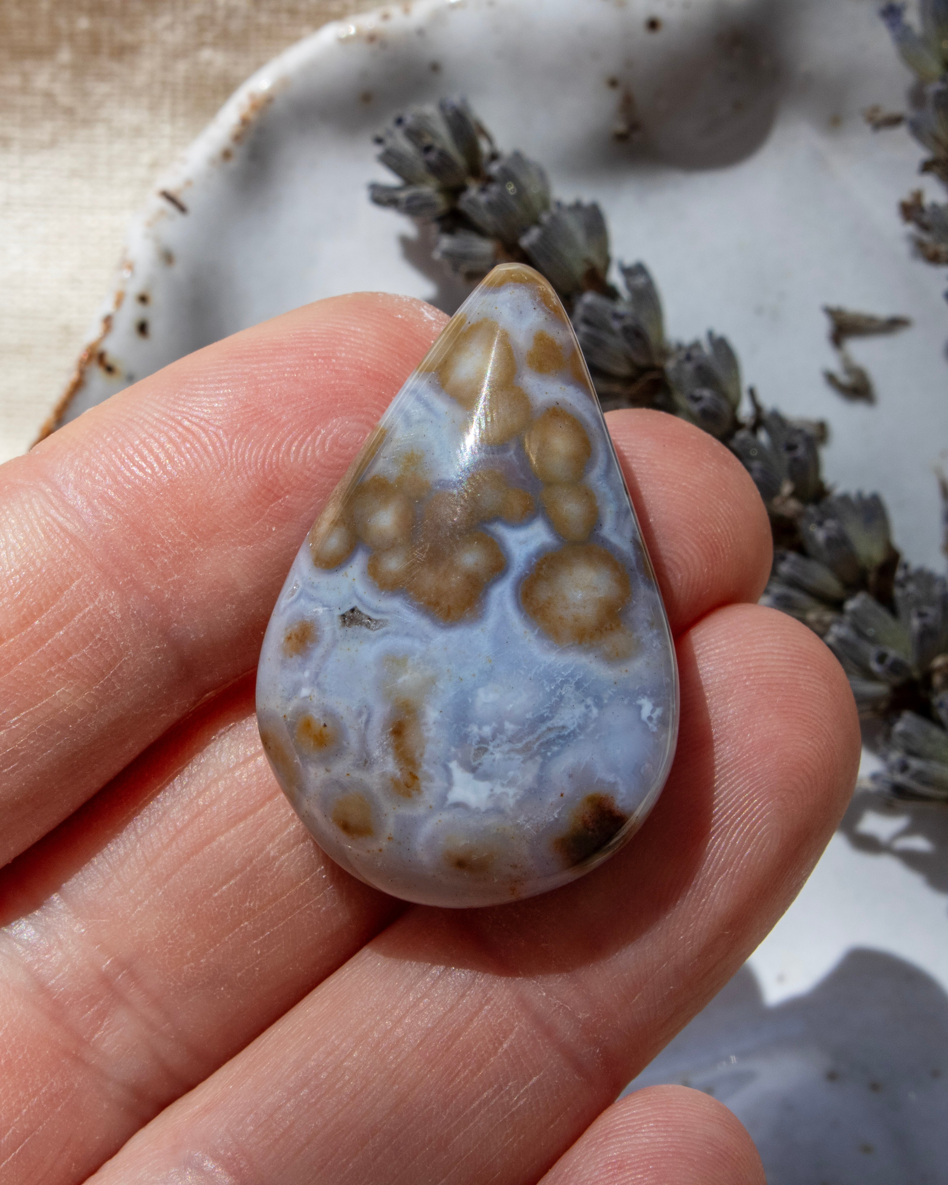 Teardrop-shaped agate stone being held with dried lavender in the background.