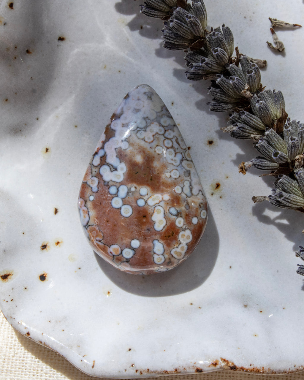 Teardrop-shaped agate stone on a textured white surface with dried lavender.