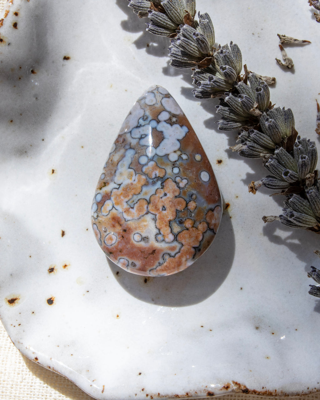 Teardrop-shaped decorative stone with a unique pattern on a textured surface with dried lavender.