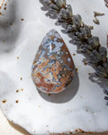 Teardrop-shaped decorative stone with a unique pattern on a textured surface with dried lavender.