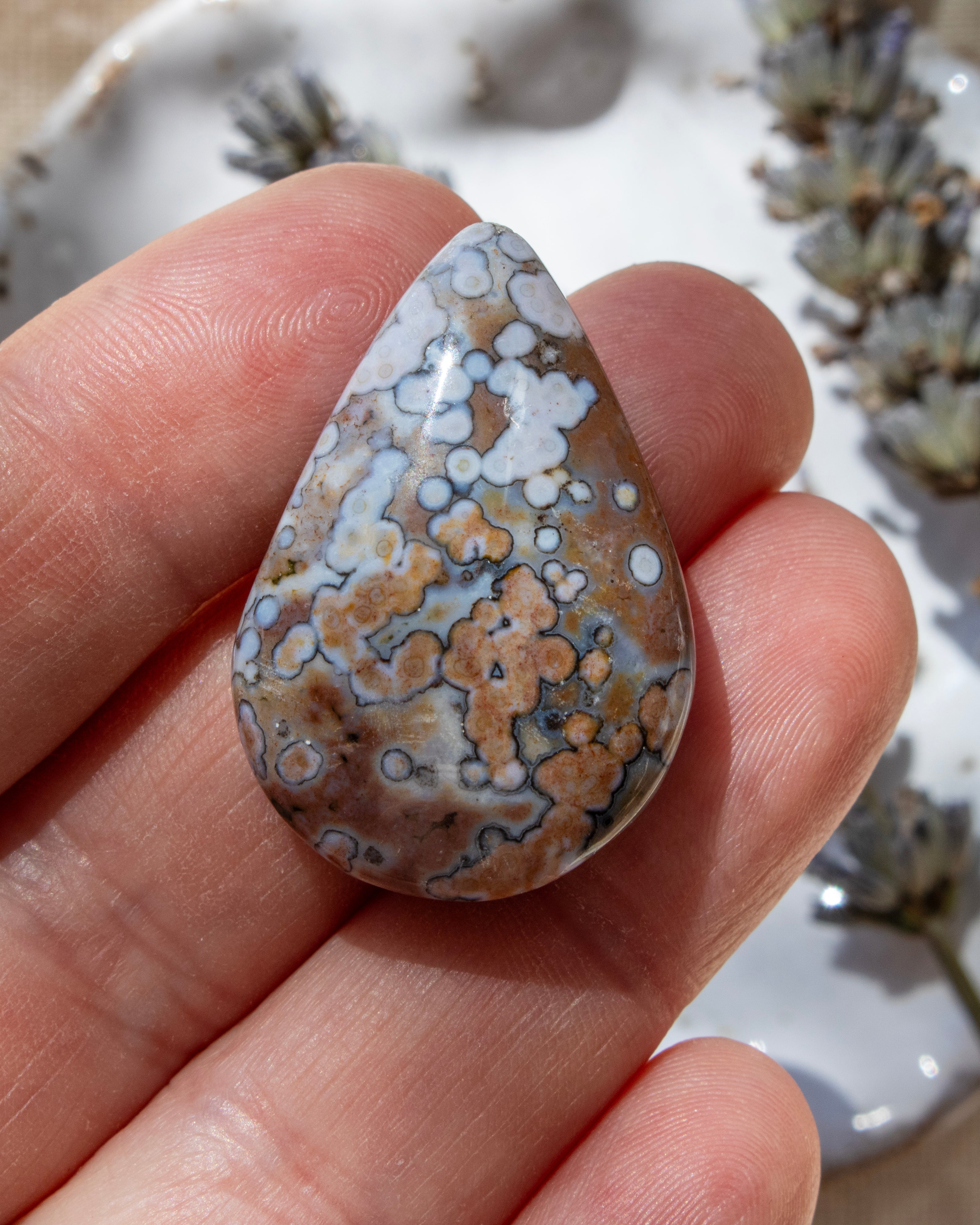 Teardrop-shaped agate stone held between fingers with a blurred natural background