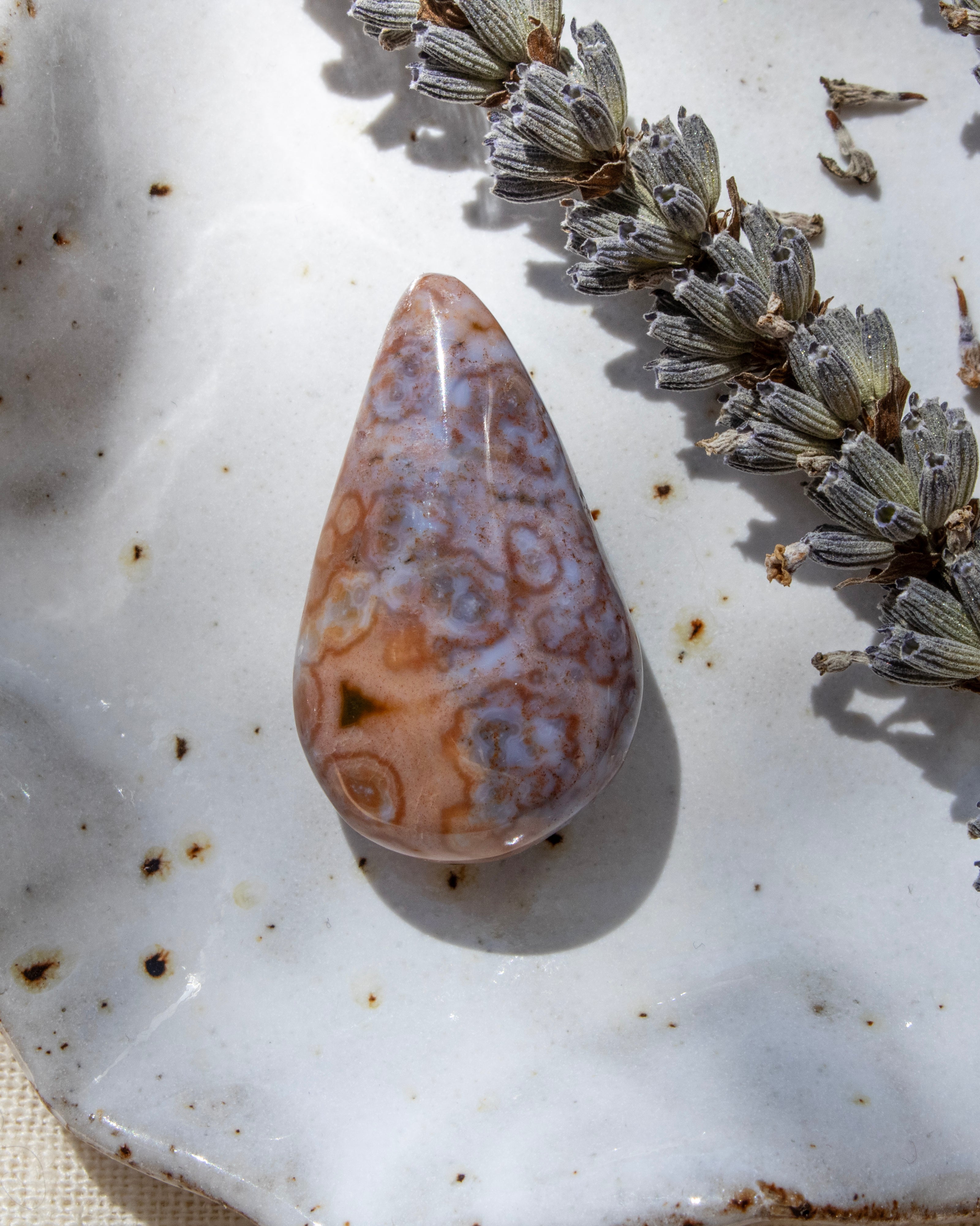 Teardrop-shaped agate stone on a textured surface with dried lavender.