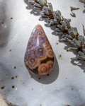 Teardrop-shaped agate stone on a textured surface with dried lavender flowers.