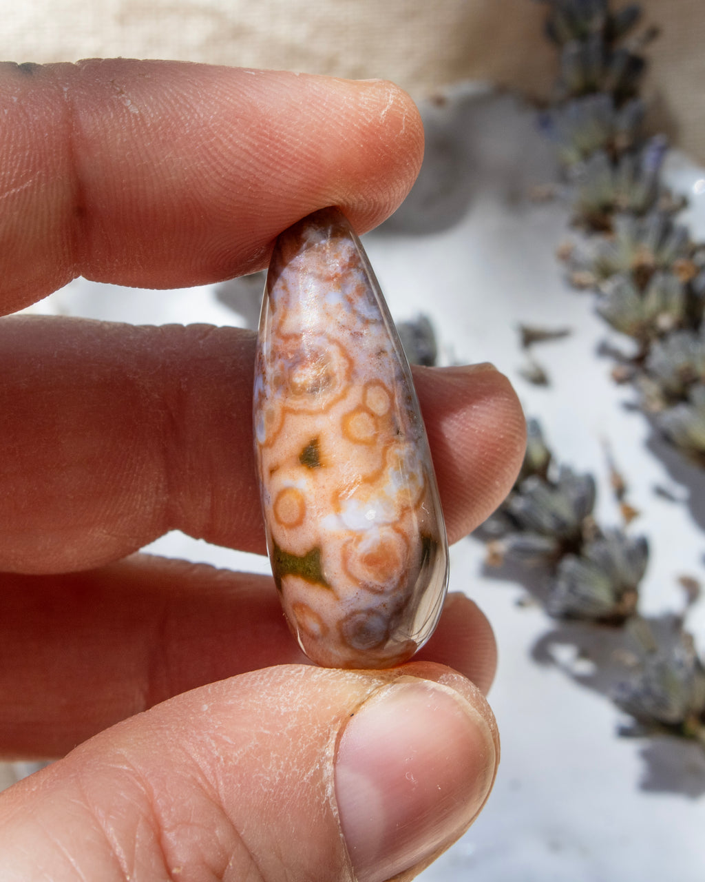 Teardrop-shaped agate stone being held with dried lavender behind.