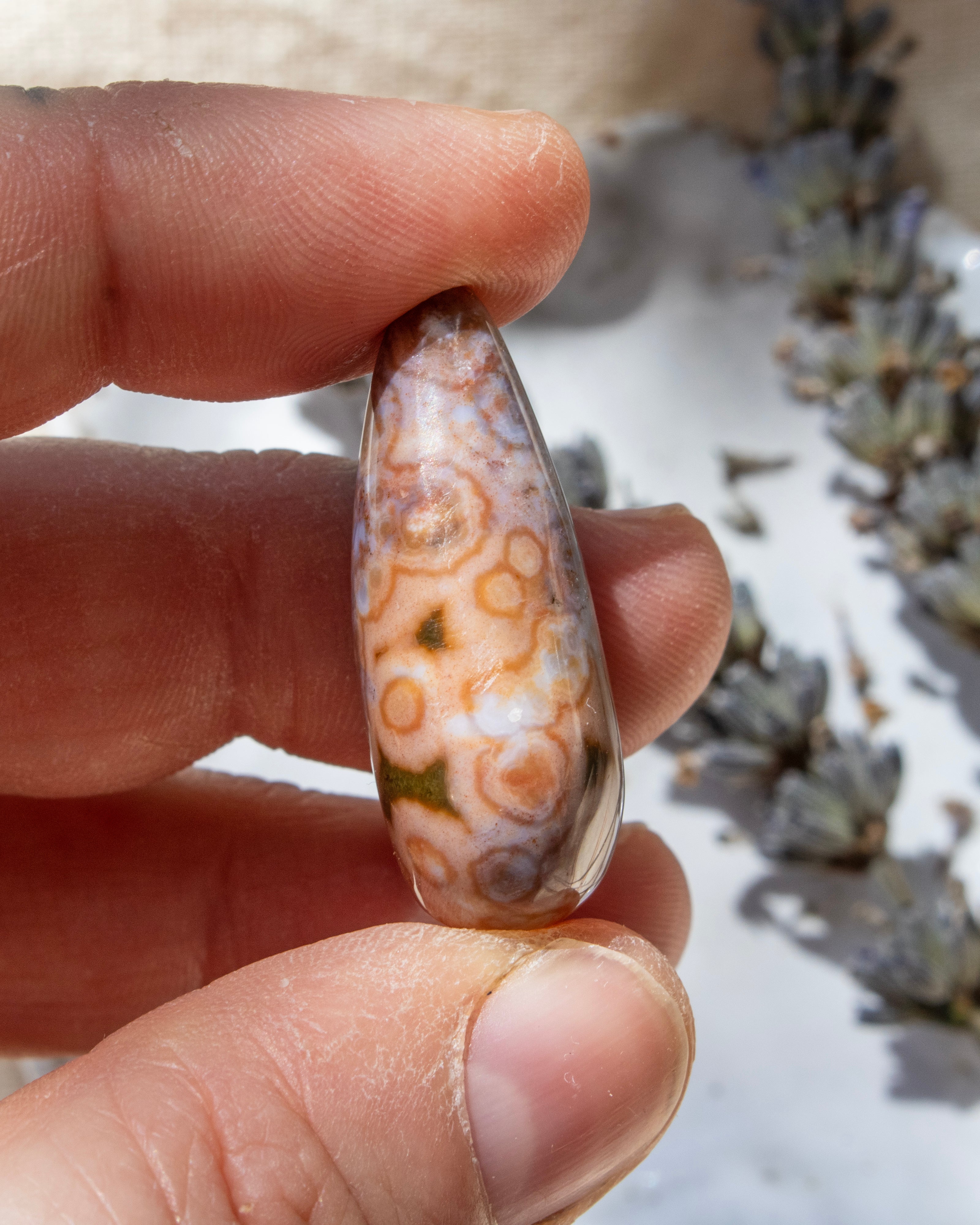 Teardrop-shaped agate stone being held with dried lavender behind.