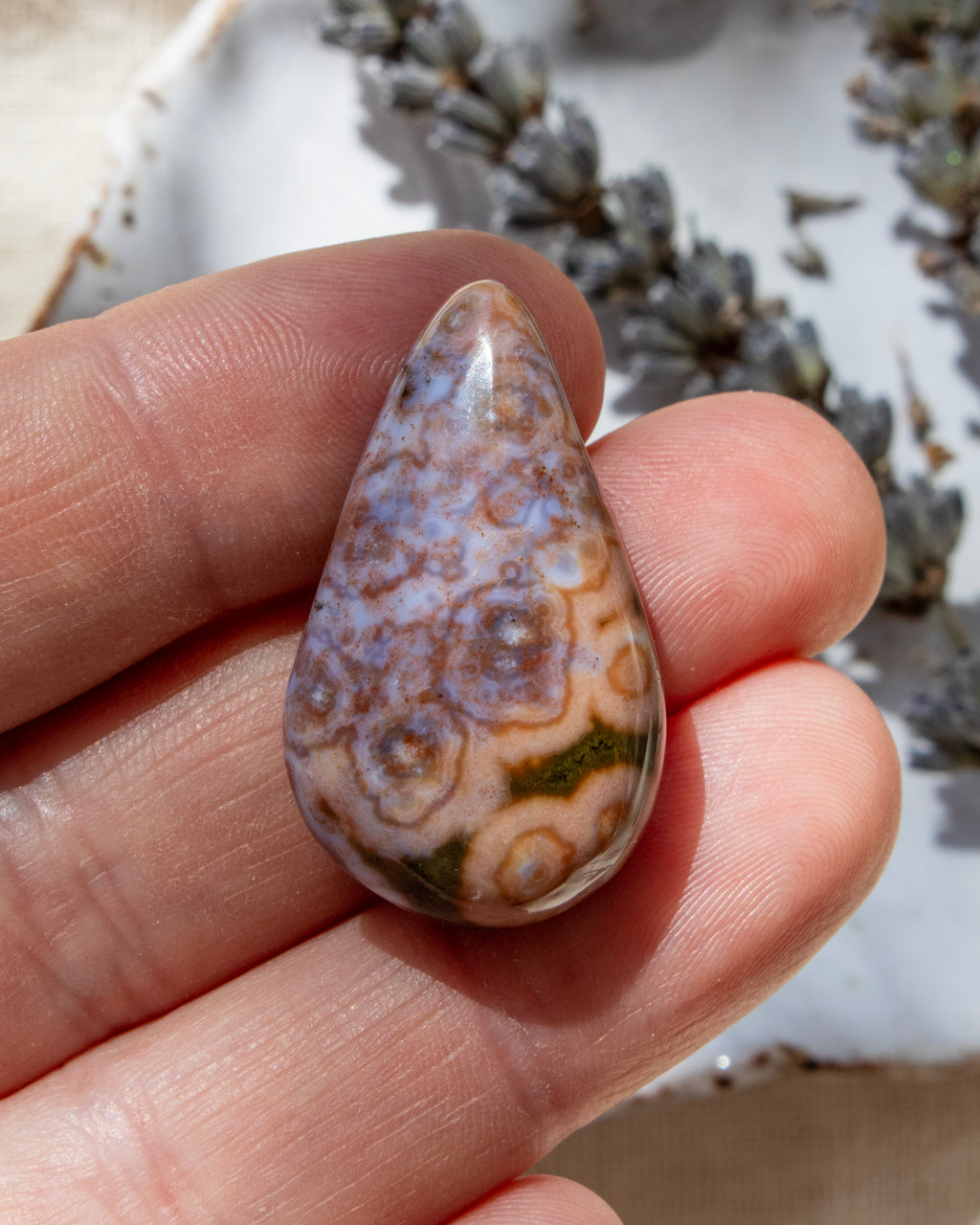 Teardrop-shaped agate stone held between fingers with a blurred natural background