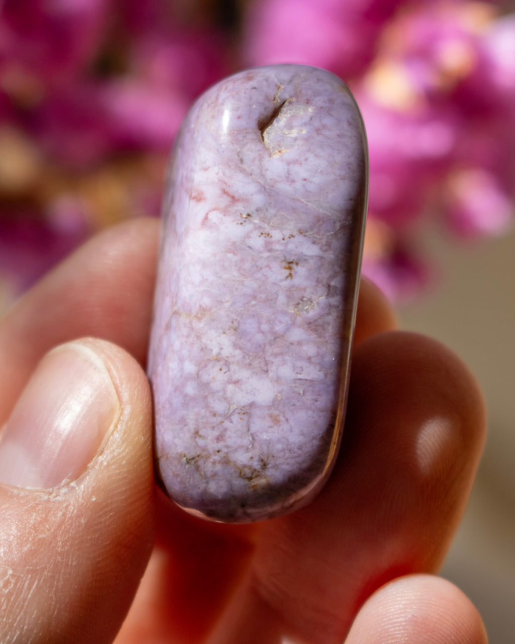 Purple stone held in a hand with a blurred pink flower background