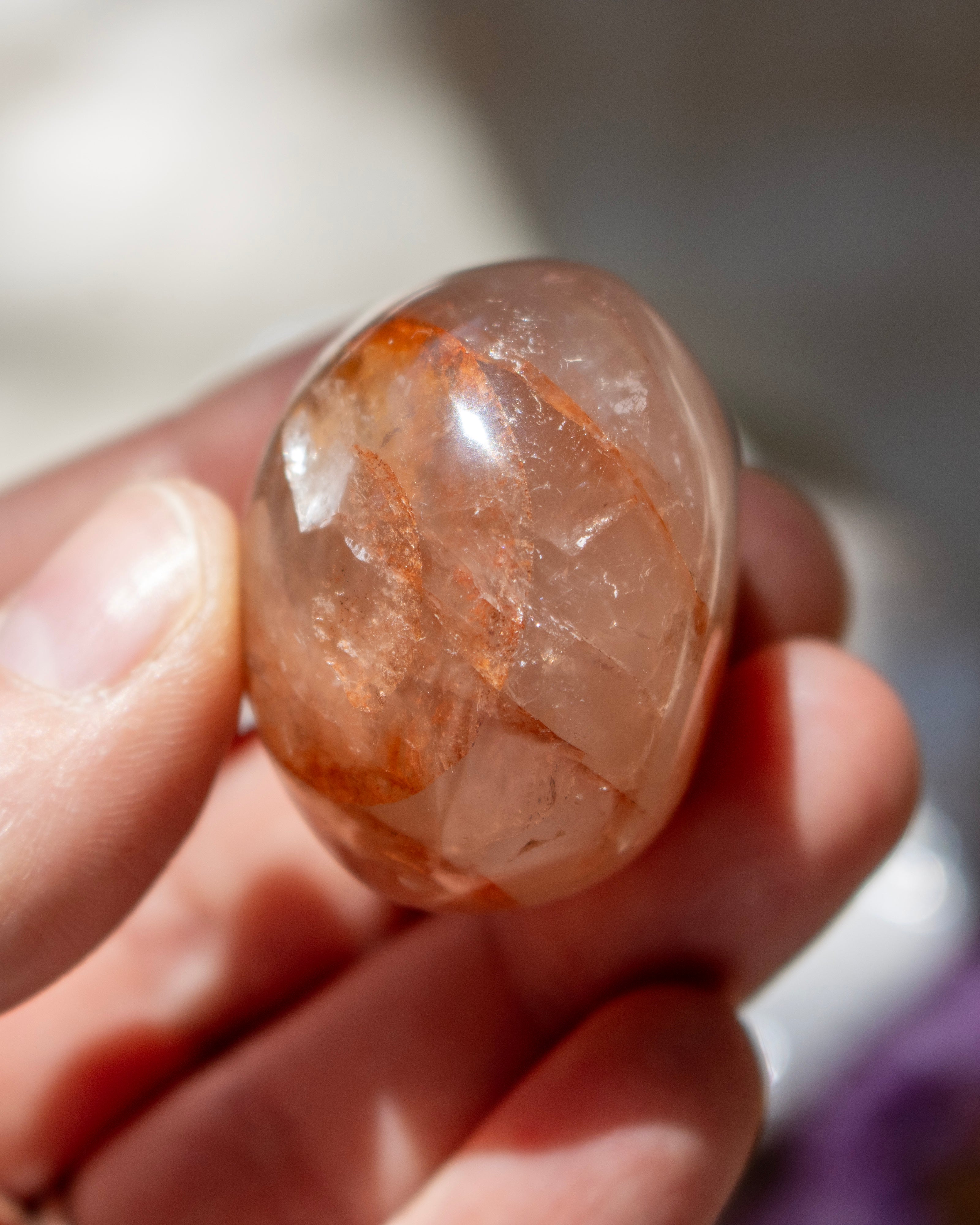 Hand holding a clear crystal with orange inclusions against a blurred background