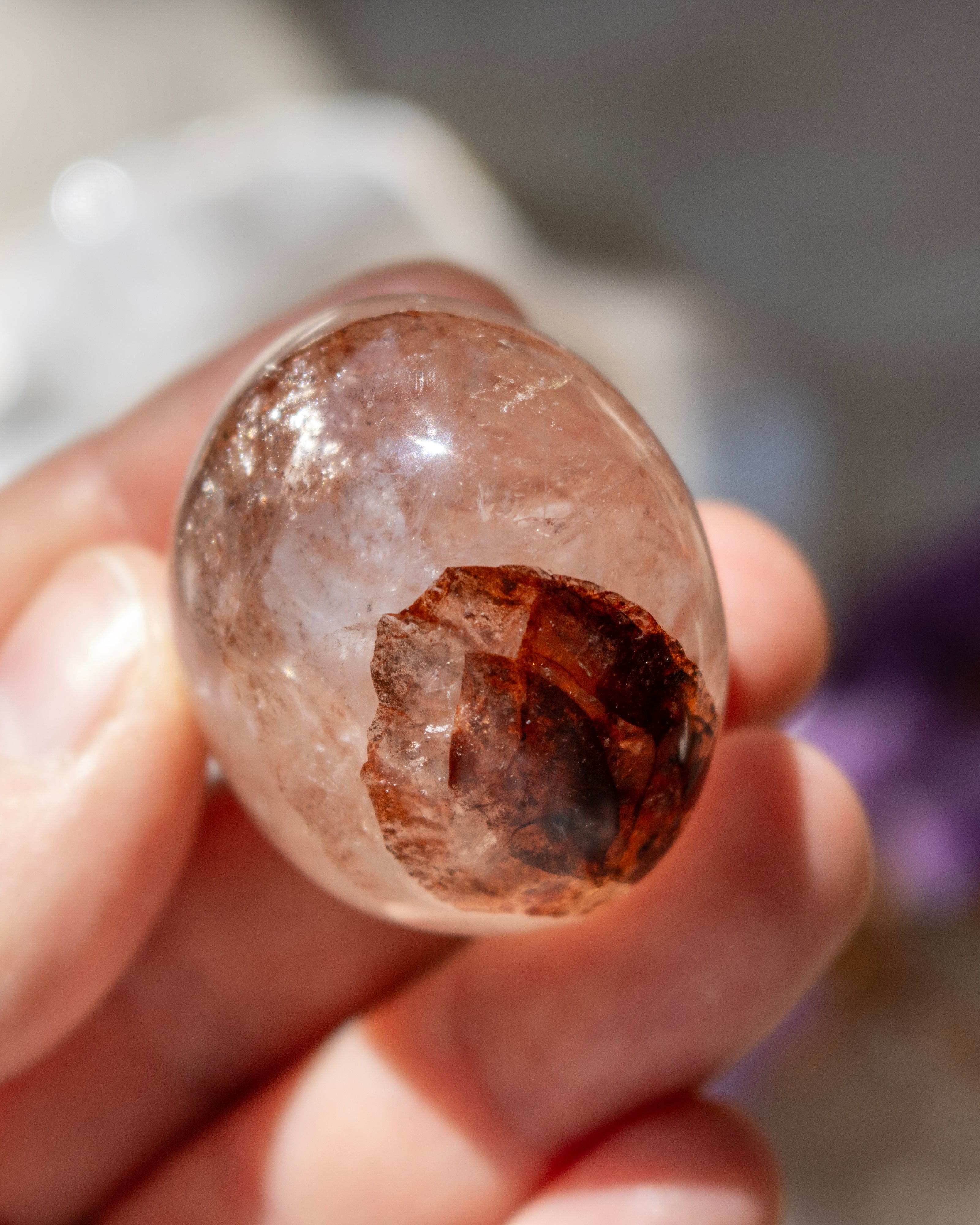 Clear crystal with brown interior held in a hand against a blurred background