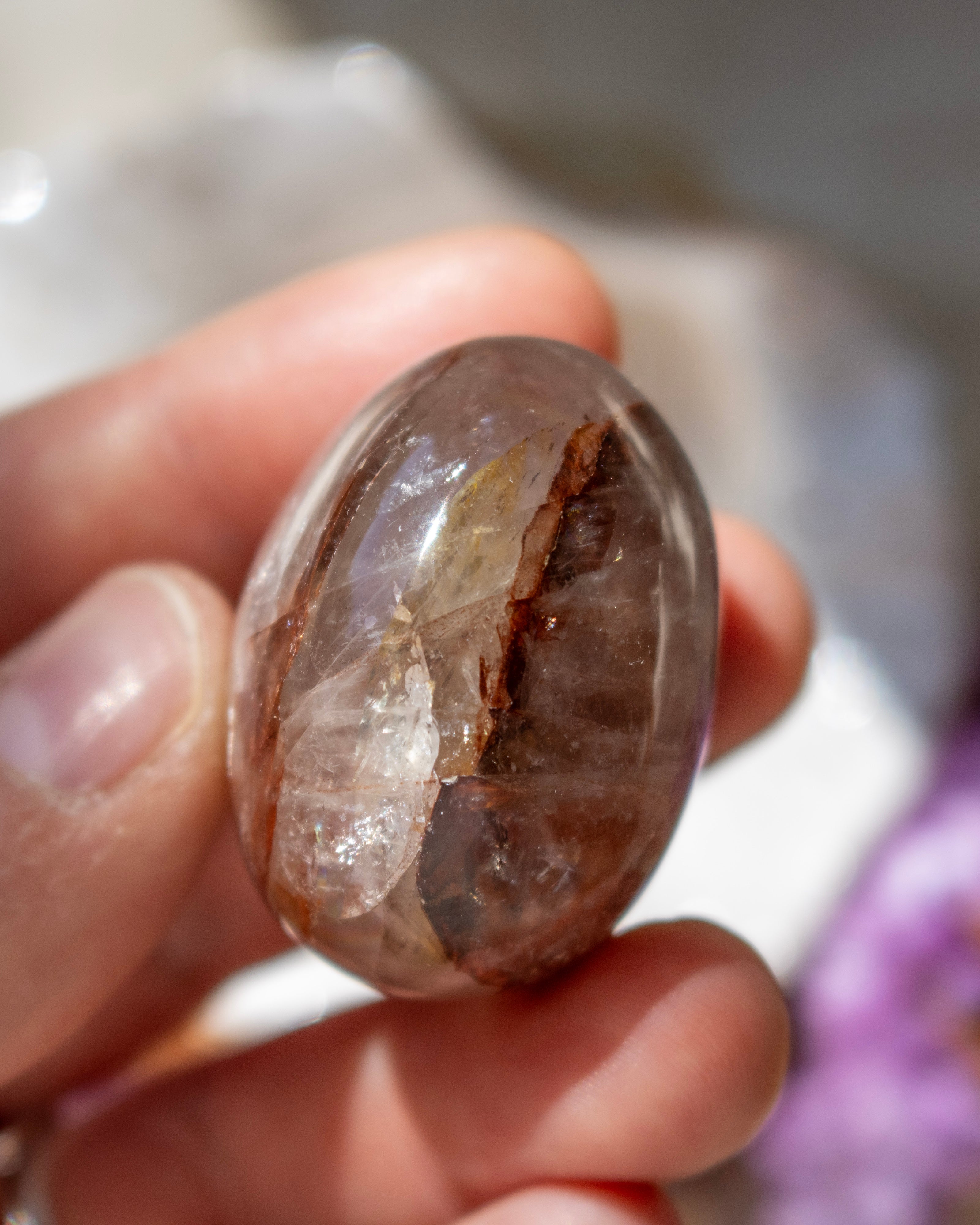 Hand holding a clear crystal with embedded stone against a blurred background