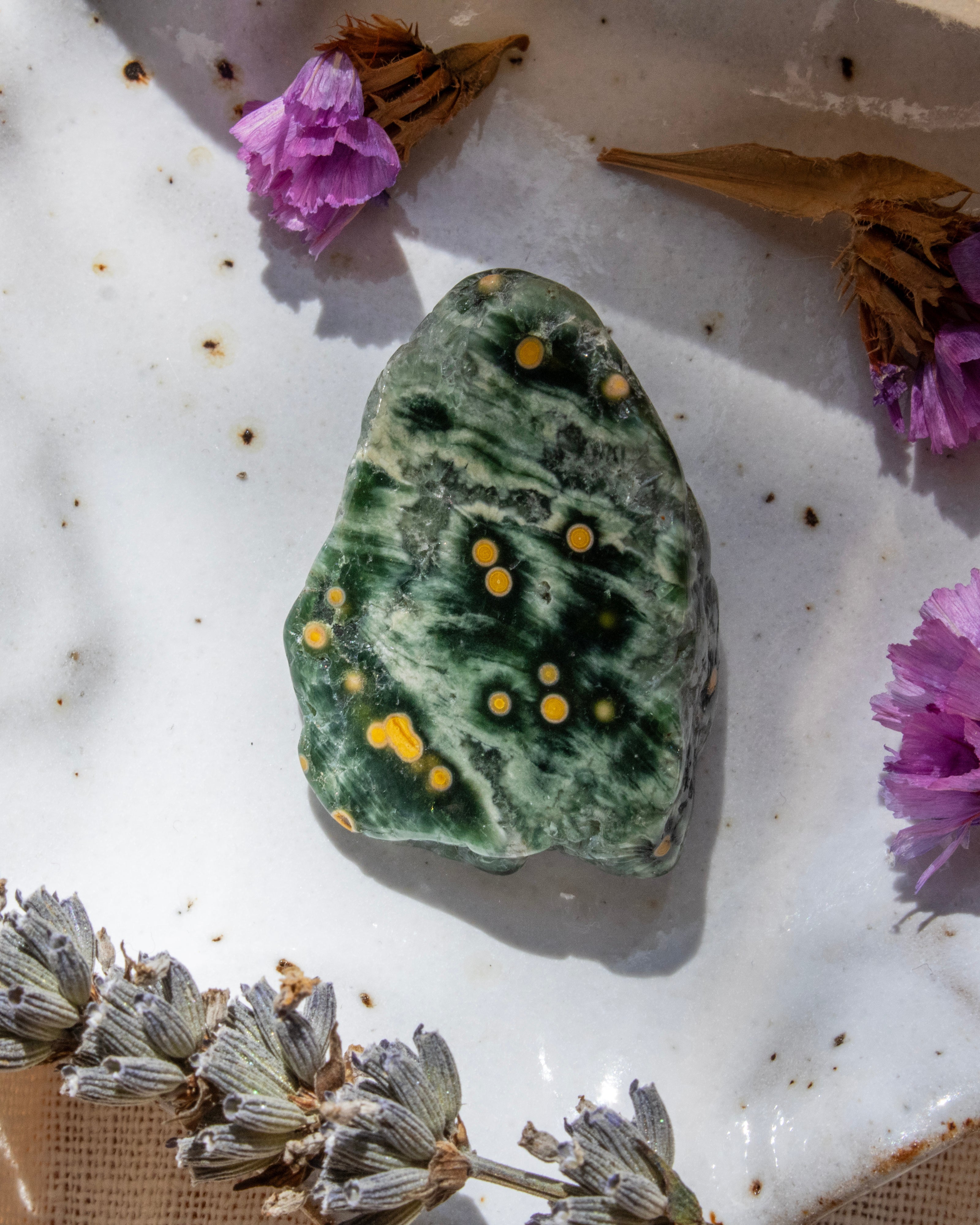 Green stone with yellow spots on a white surface with dried flowers and herbs