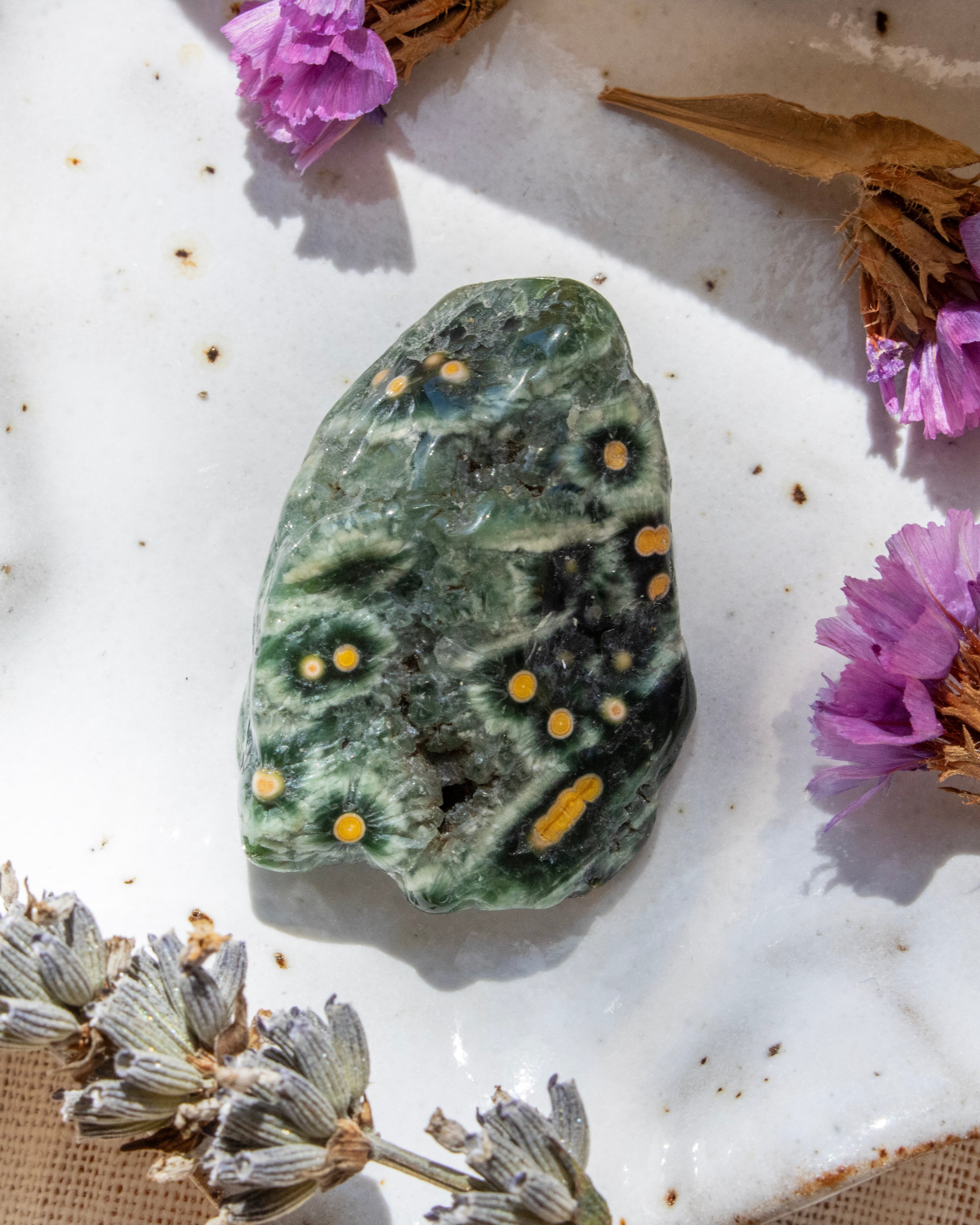 Green marbled stone with yellow spots on a white surface with dried flowers