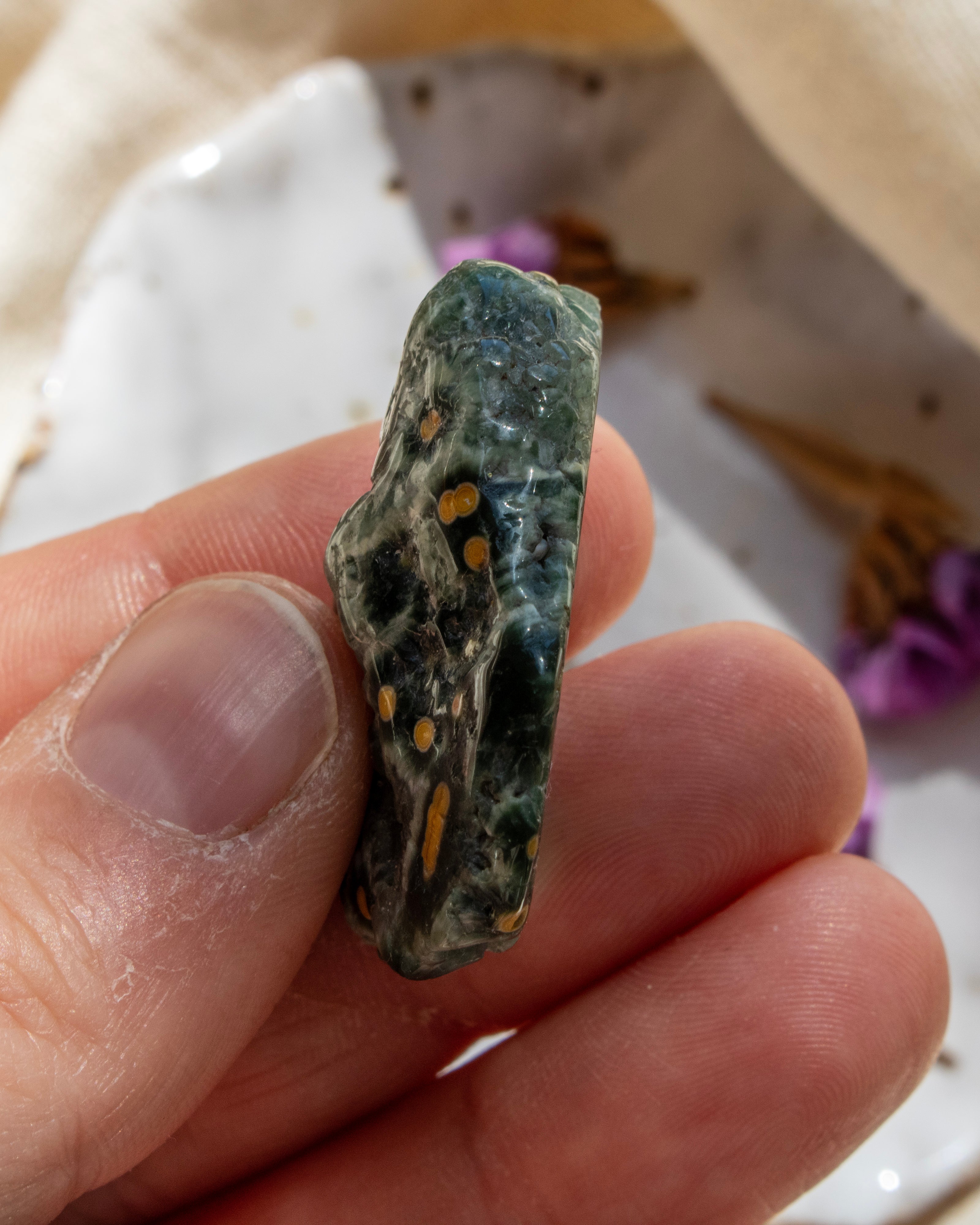 Hand holding a rough stone with visible minerals, blurred background
