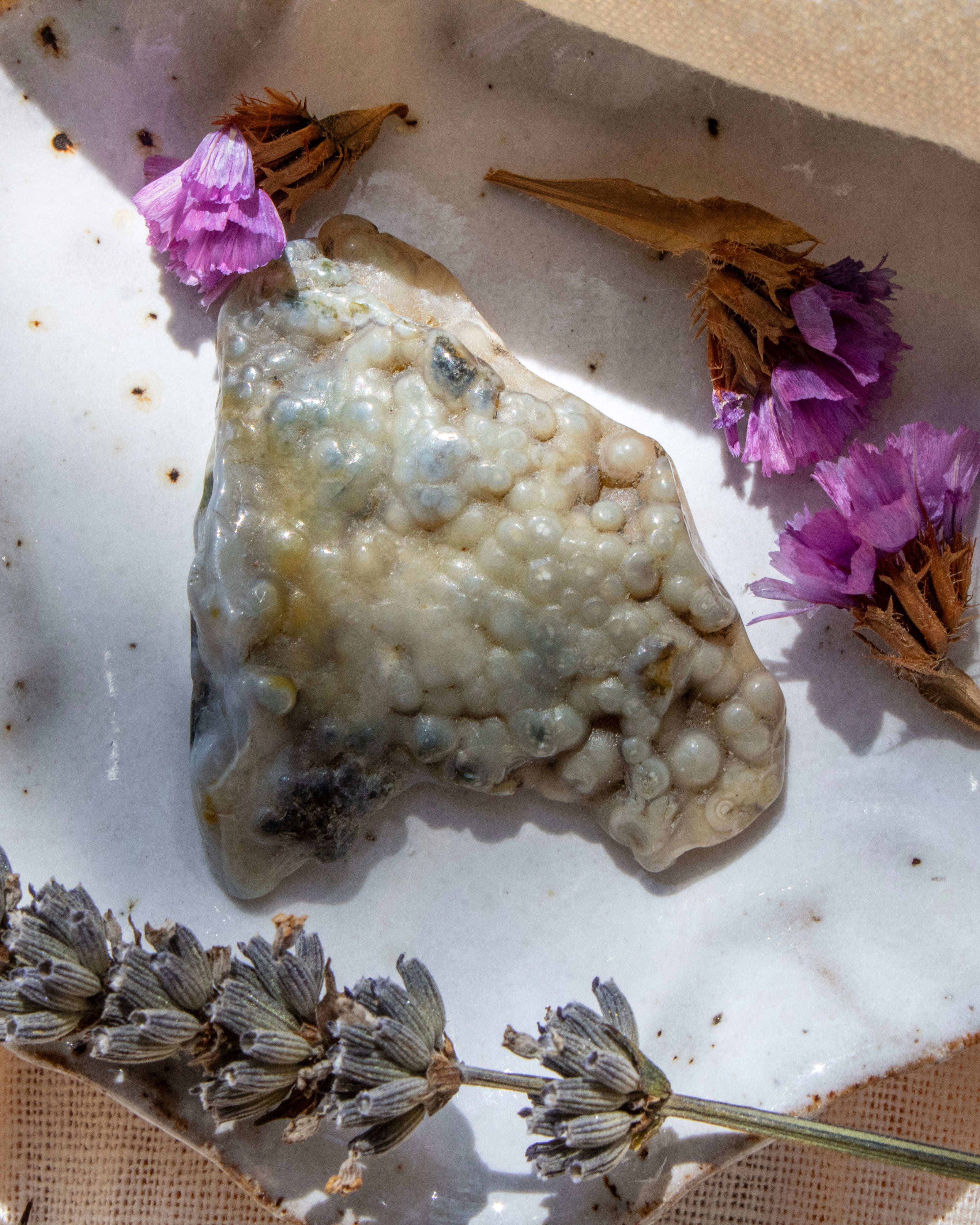 Marble surface with a textured stone, dried flowers, and lavender leaves.