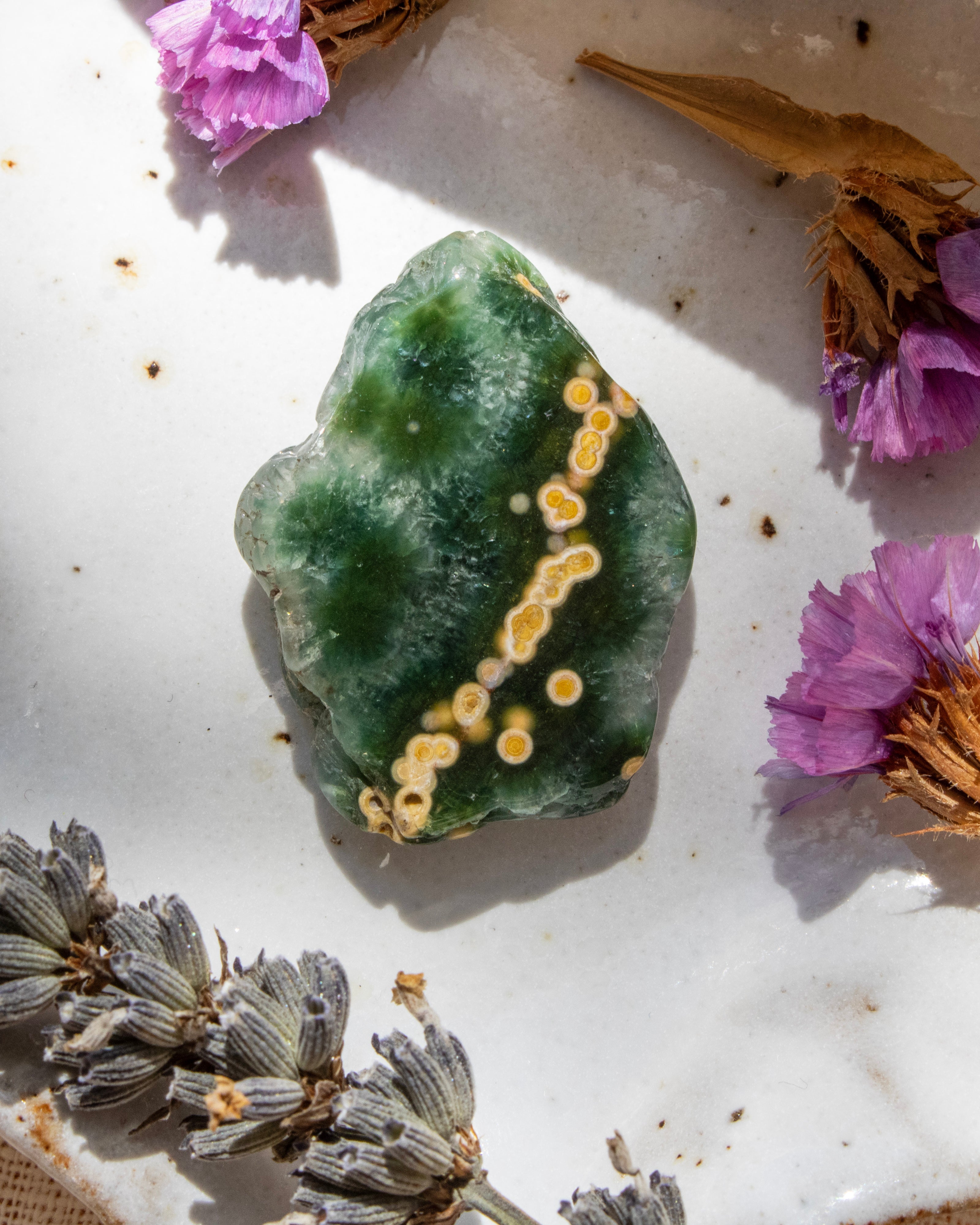 Green crystal with yellow markings on a white surface with dried flowers