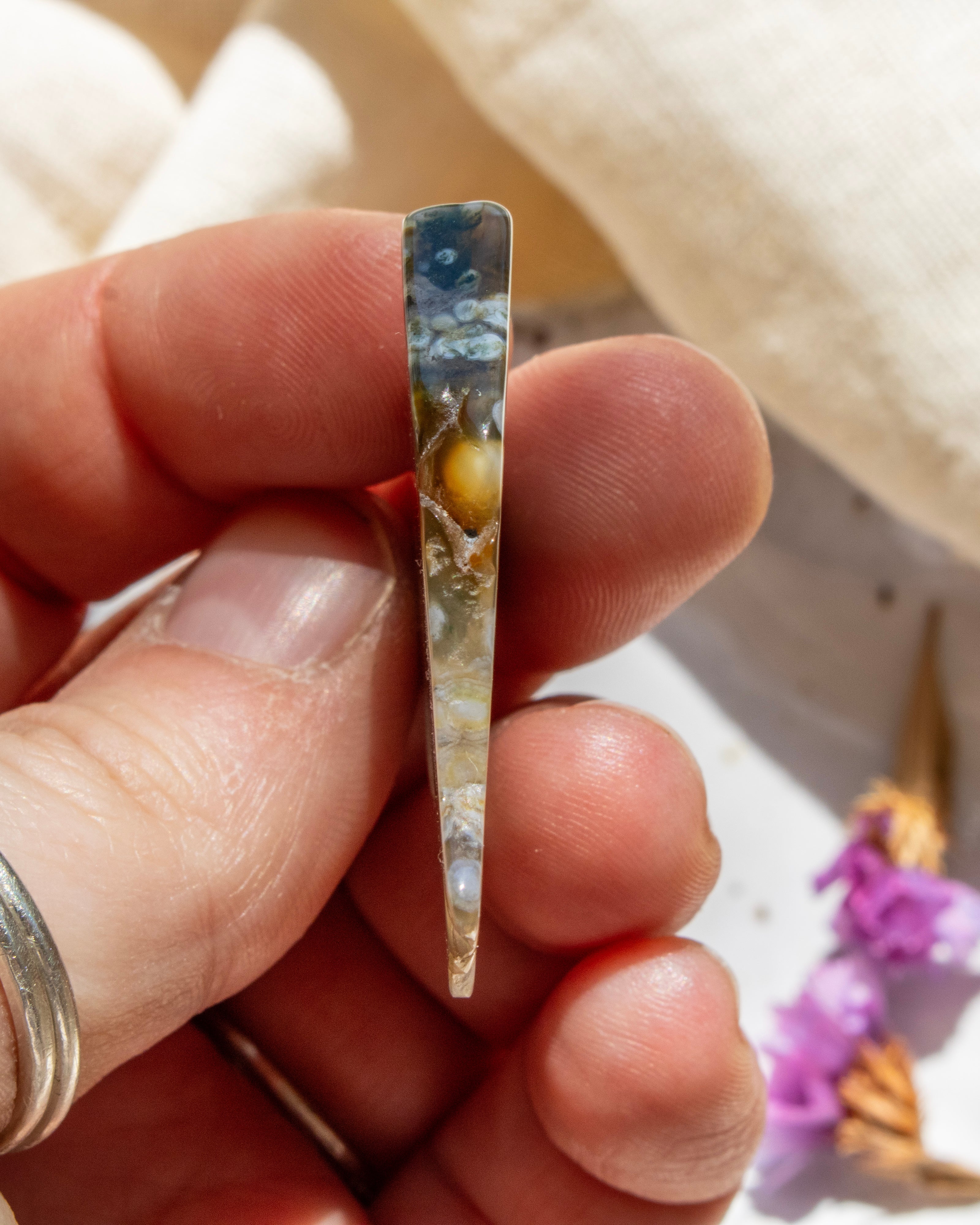 Hand holding a small, thin piece of jewelry with a scenic design.
