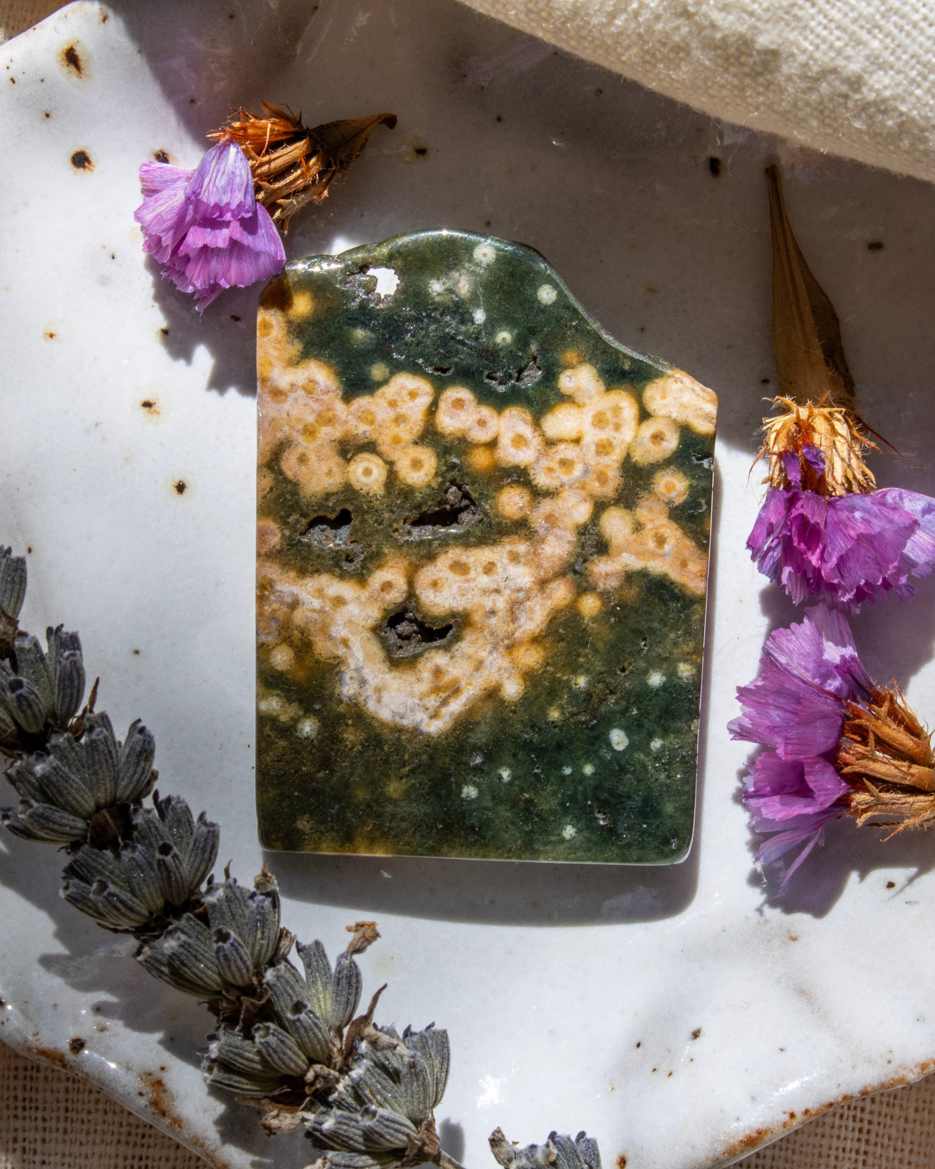 Decorative stone with a textured surface surrounded by dried flowers on a white fabric background