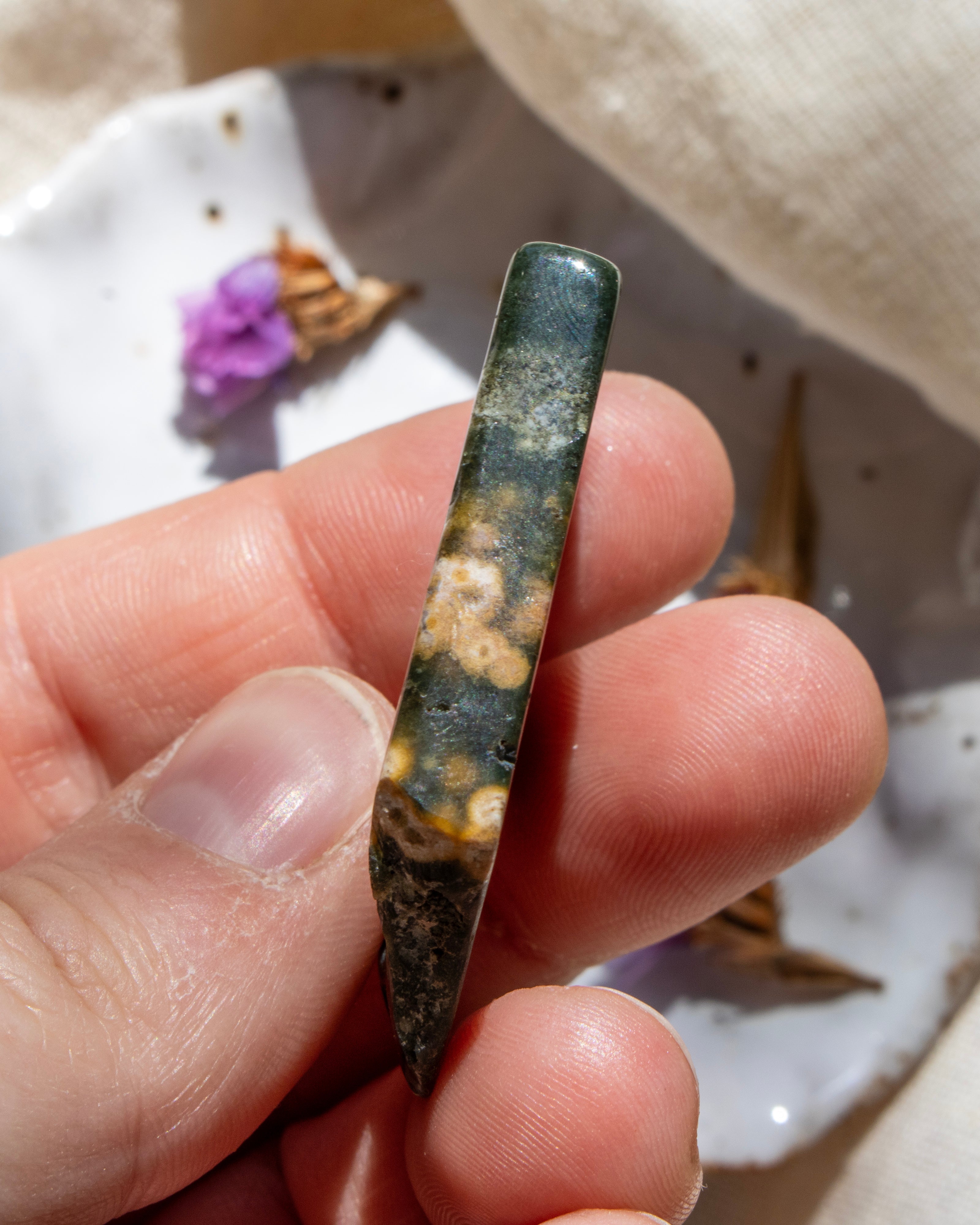 Hand holding a green and brown patterned stone with a blurred background