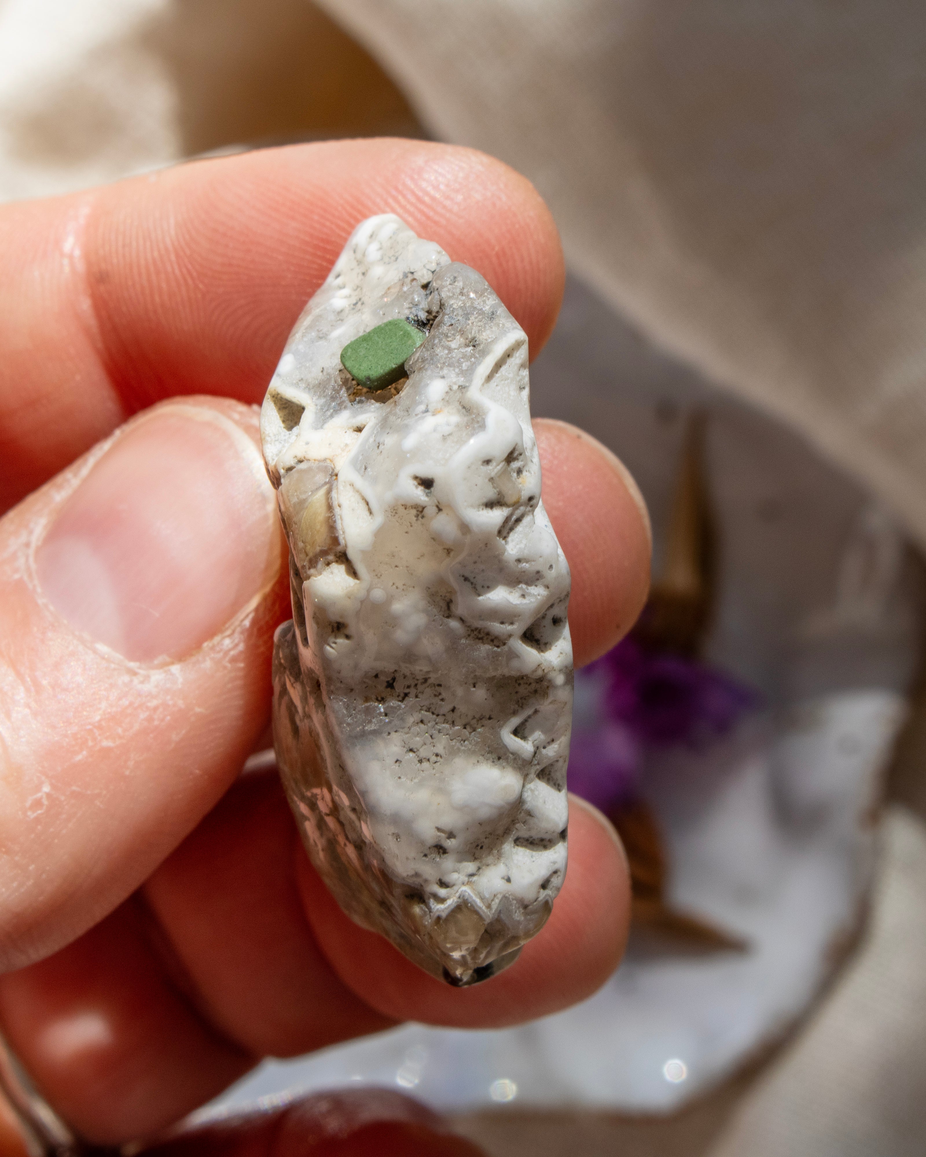 Hand holding a stone with a green mineral, blurred background