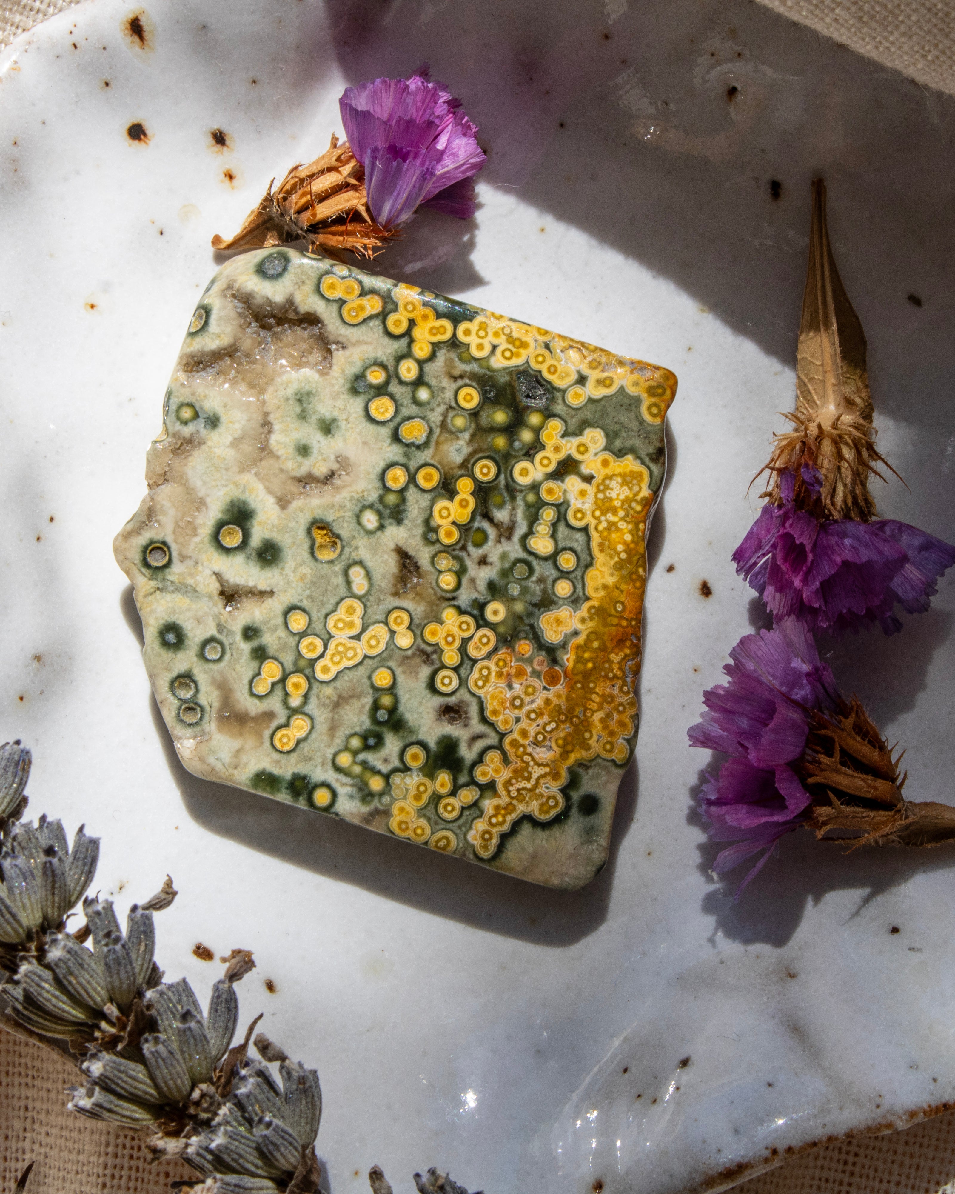 Decorative stone with yellow and green patterns on a white surface with dried flowers.