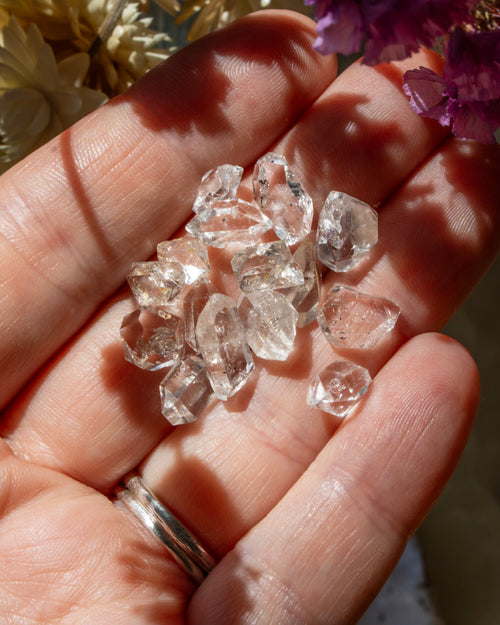 Hand holding clear crystal stones with a blurred floral background