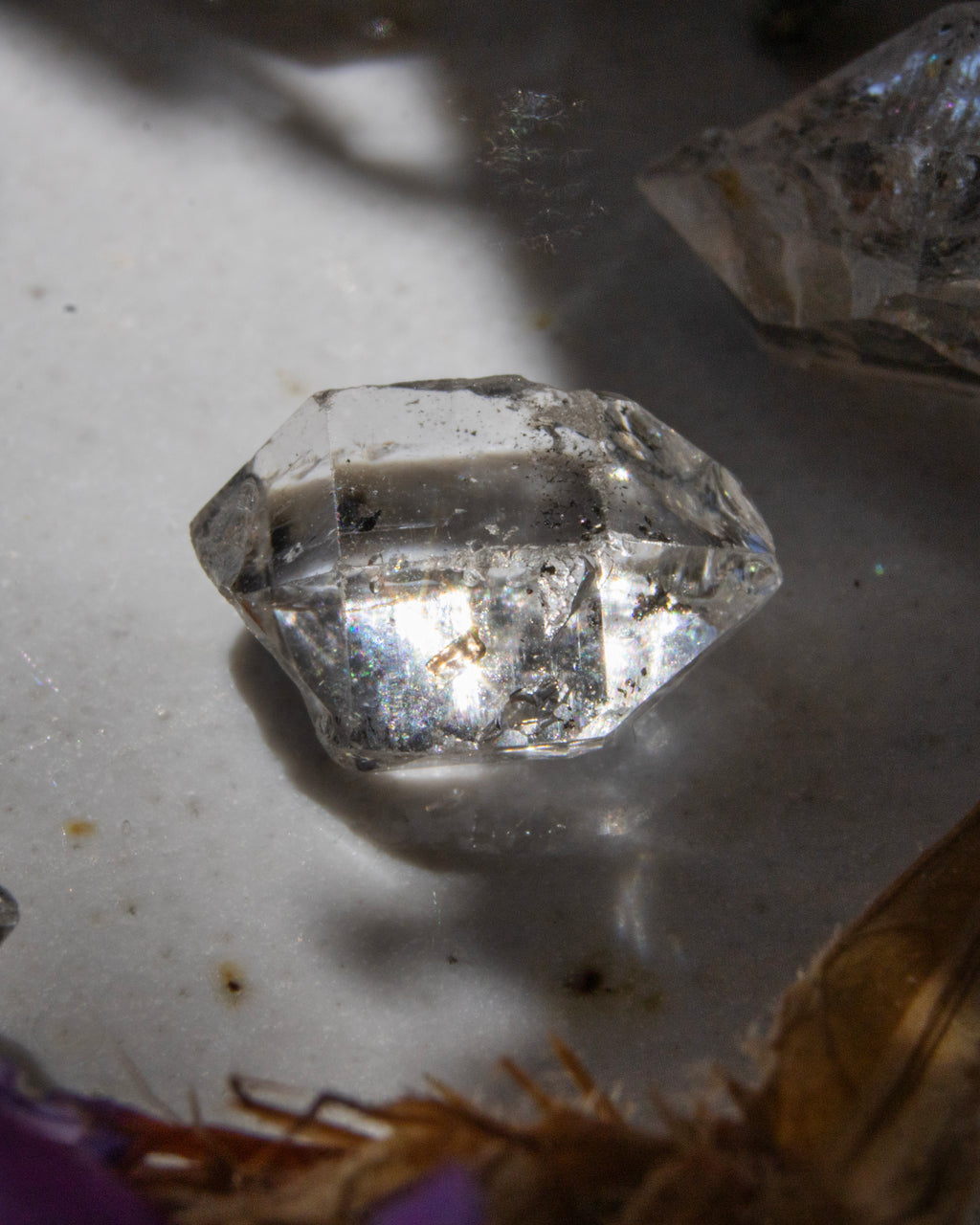 Clear crystal on a light gray surface with a purple object partially visible