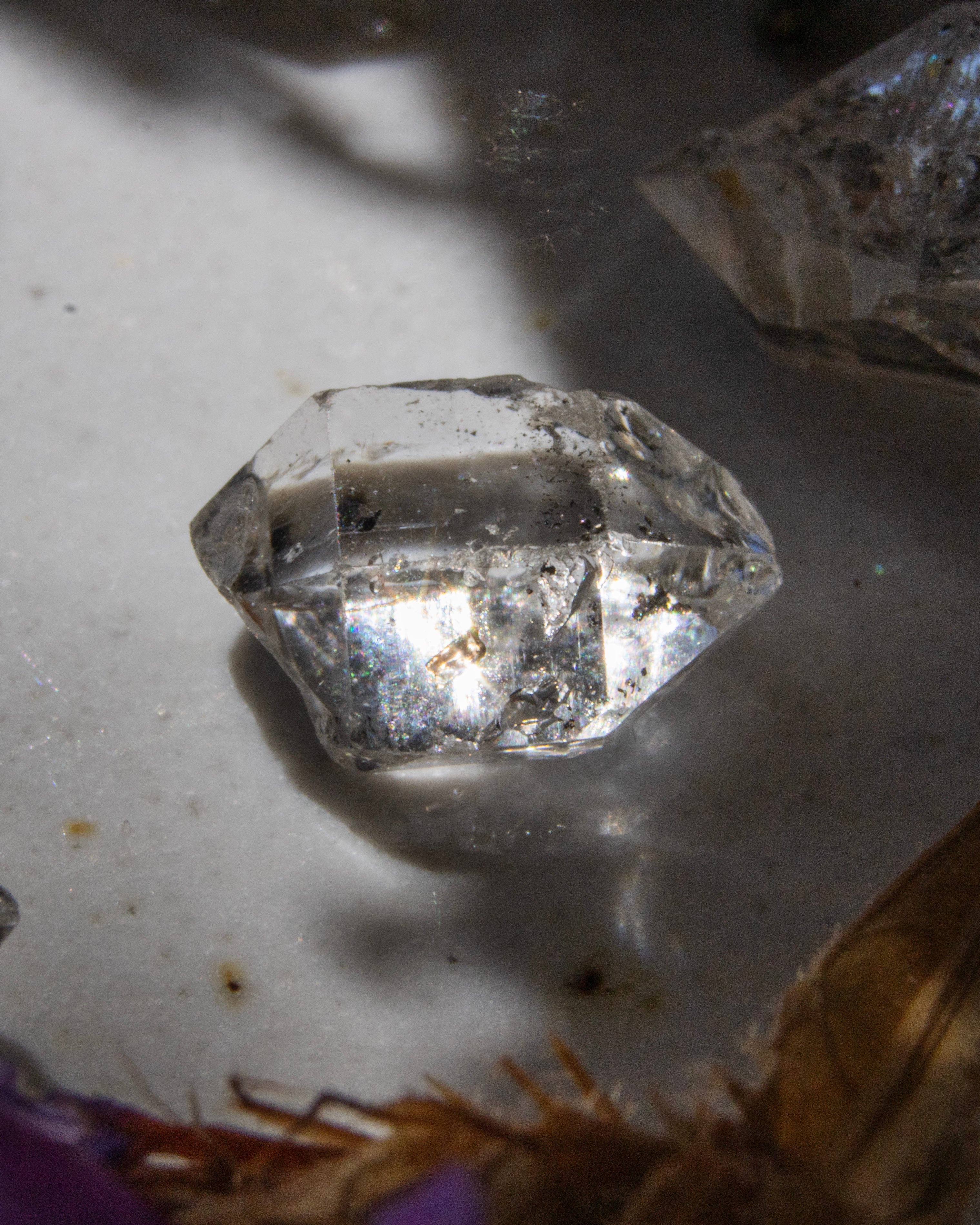 Clear crystal on a light gray surface with a purple object partially visible