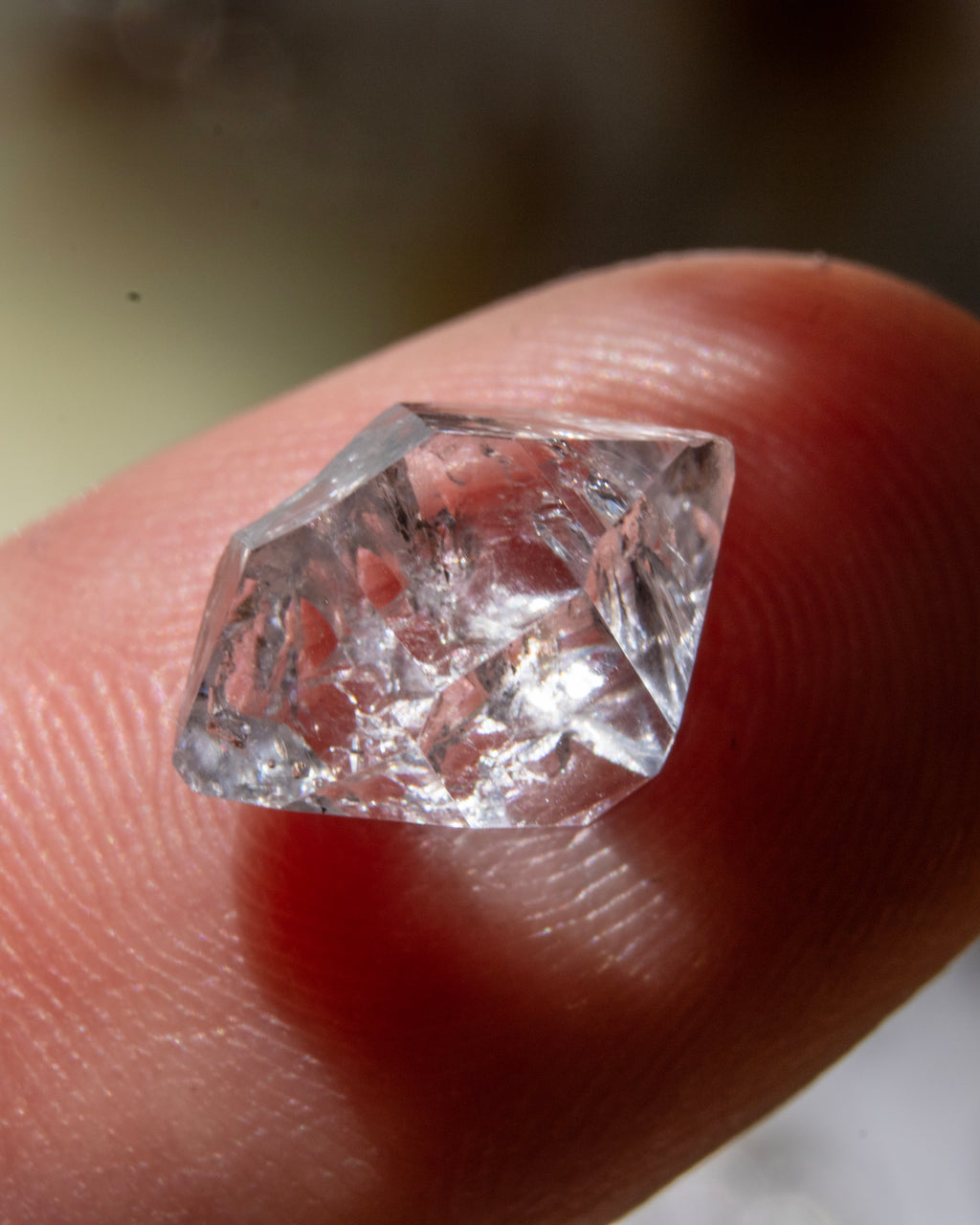 Raw diamond held between fingers against a neutral background