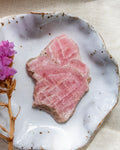 Thin slice of pink stone on a white ceramic plate with a pink flower and dried plant.