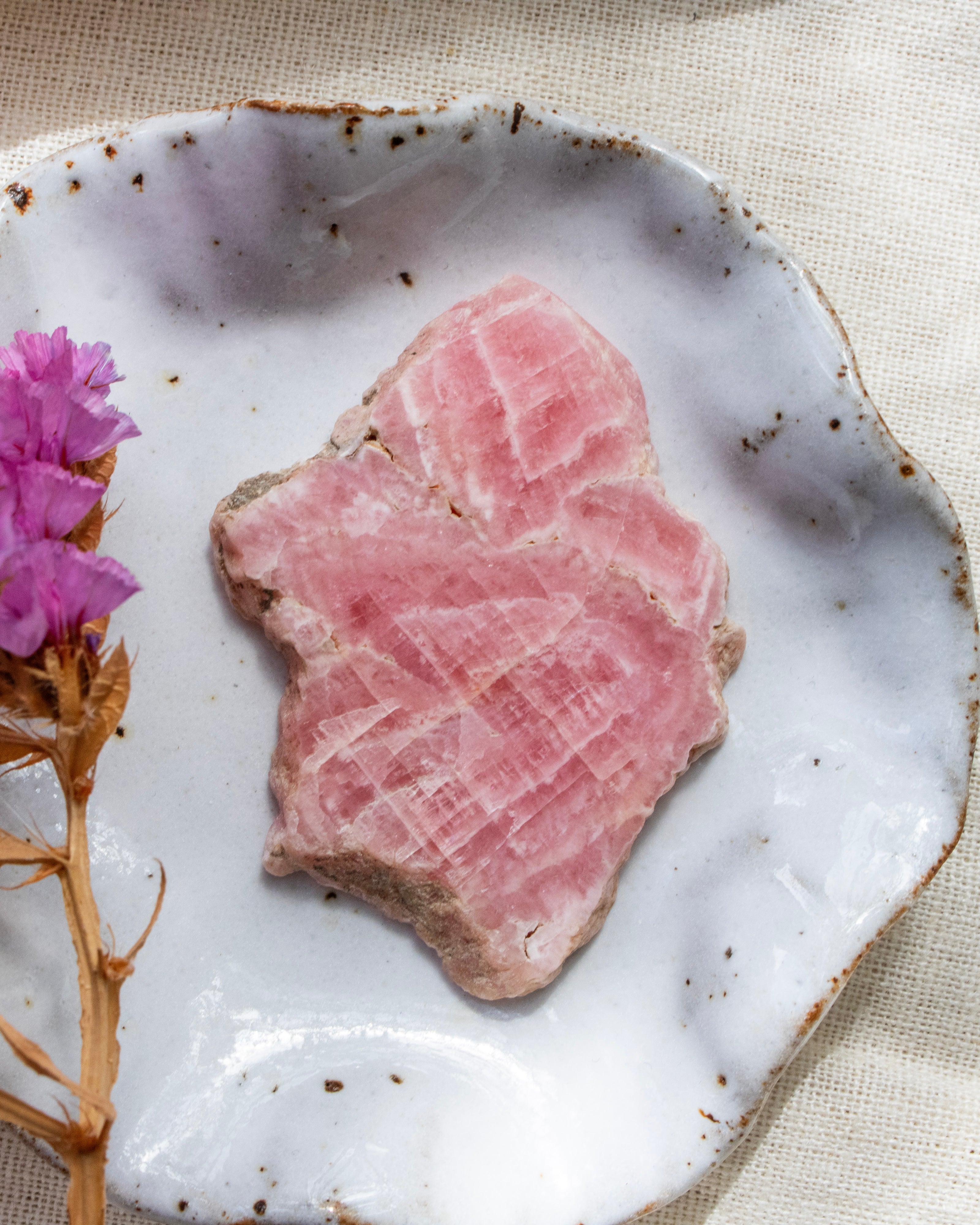 Thin slice of pink stone on a white ceramic plate with a pink flower and dried plant.