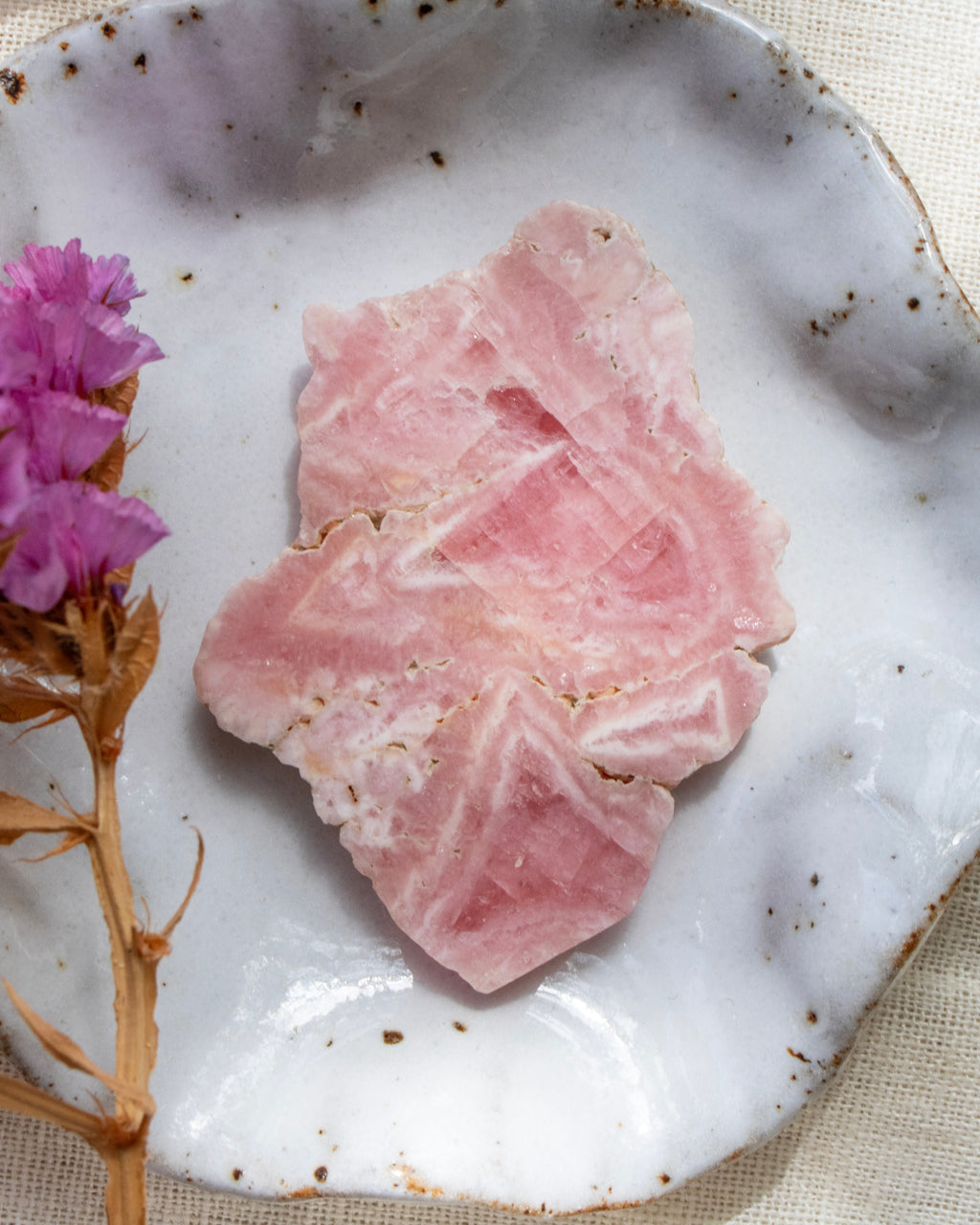 pink crystal slice on a speckled ceramic plate with a pink flower.
