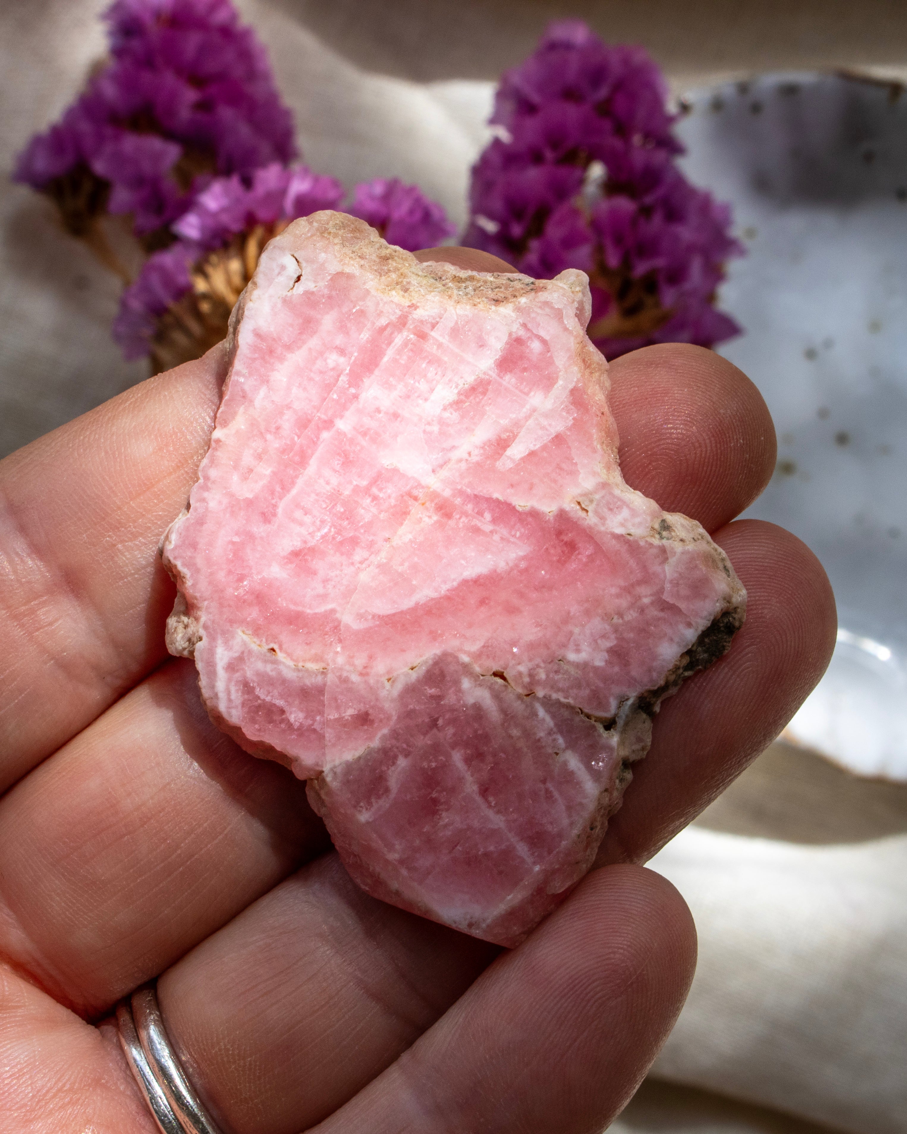 Hand holding a pink crystal with purple flowers in the background