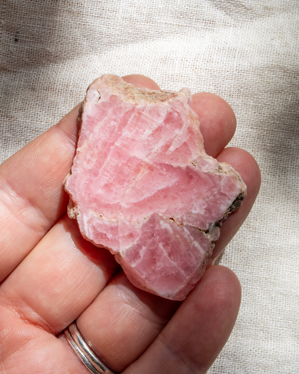 Hand holding a pink crystal rock against a textured beige background