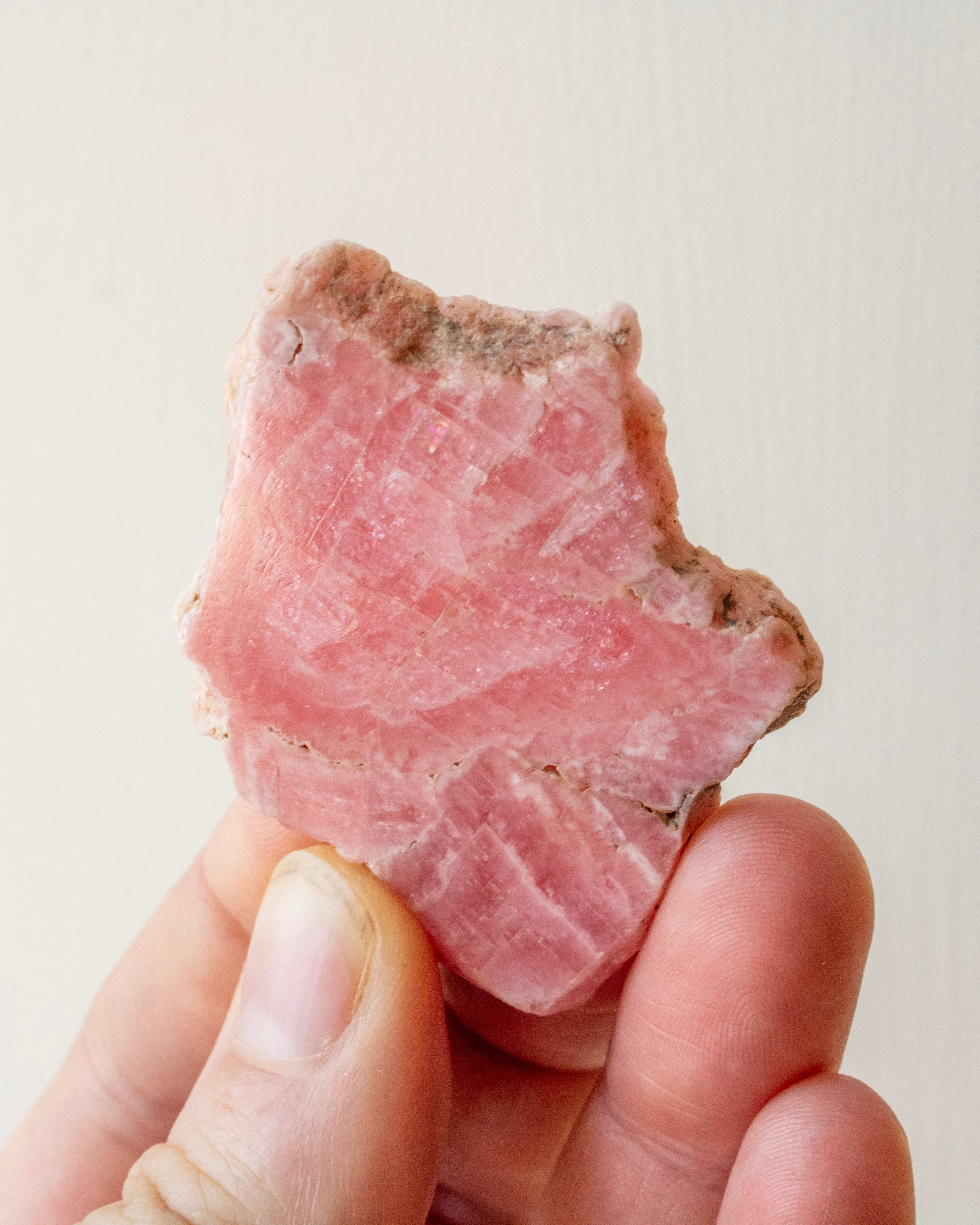 Hand holding a pink crystal against a light background
