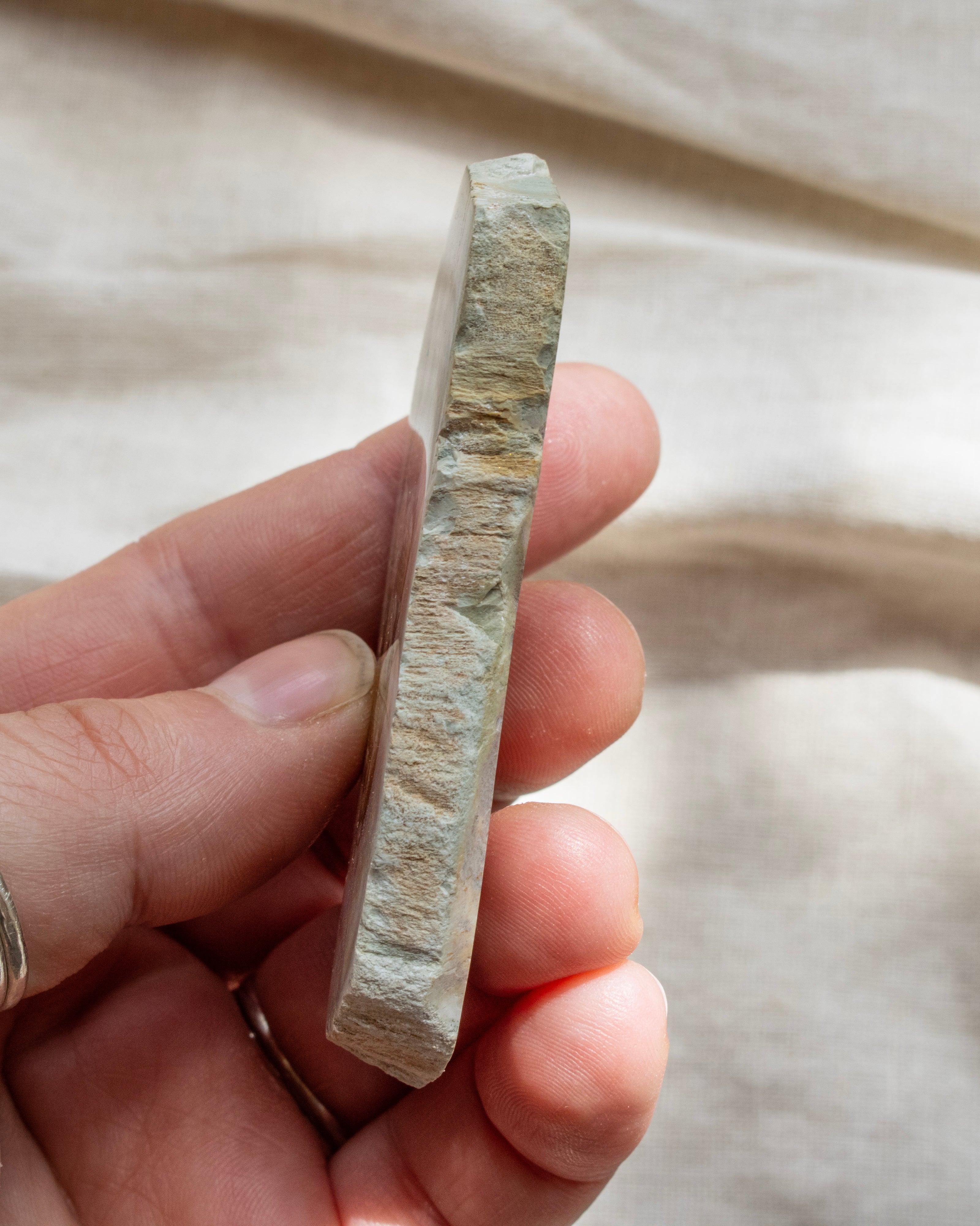 Hand holding a rectangular piece of stone or crystal against a neutral background