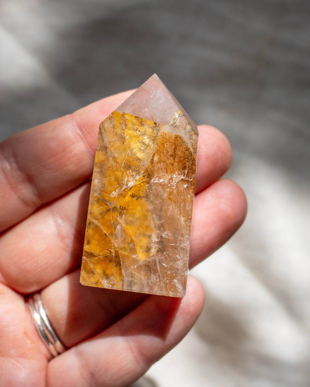 Hand holding a crystal with yellow and clear patterns against a blurred background