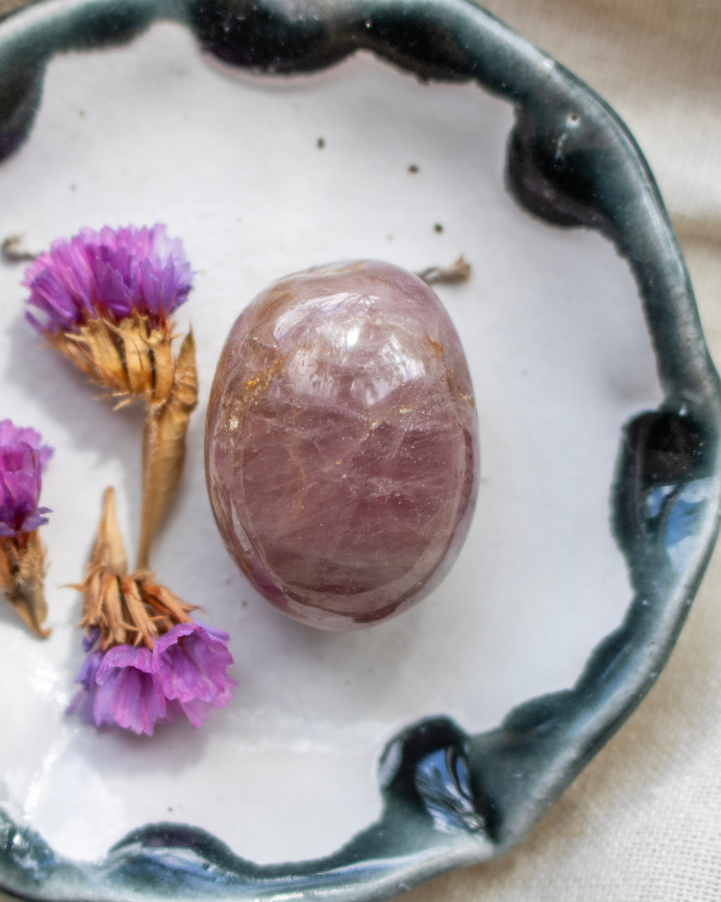 Purple crystal stone on a white surface with dried flowers