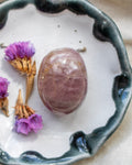 Purple crystal stone on a white surface with dried flowers