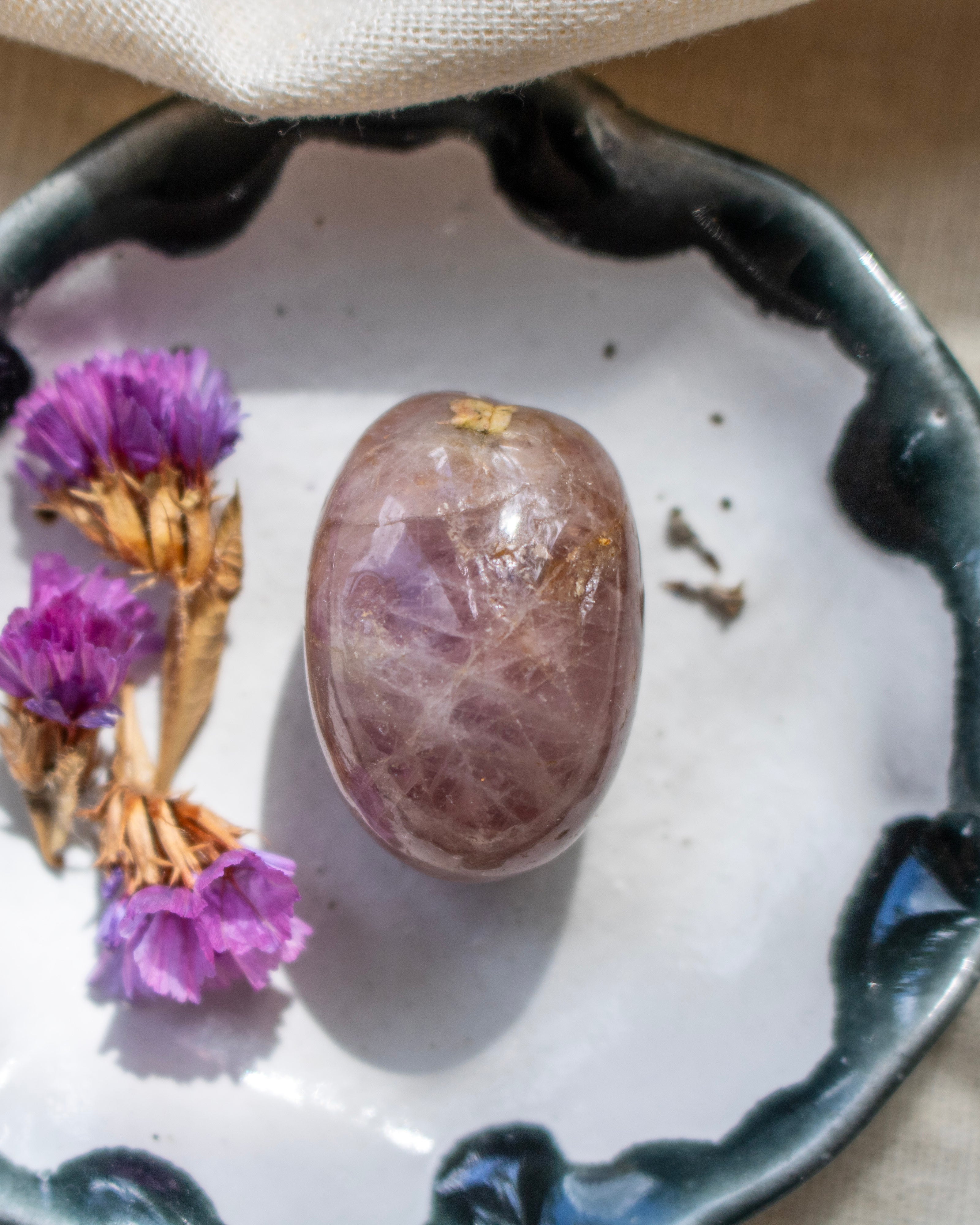 Decorative dish with a dark pink stone and dried flowers on a textured surface.