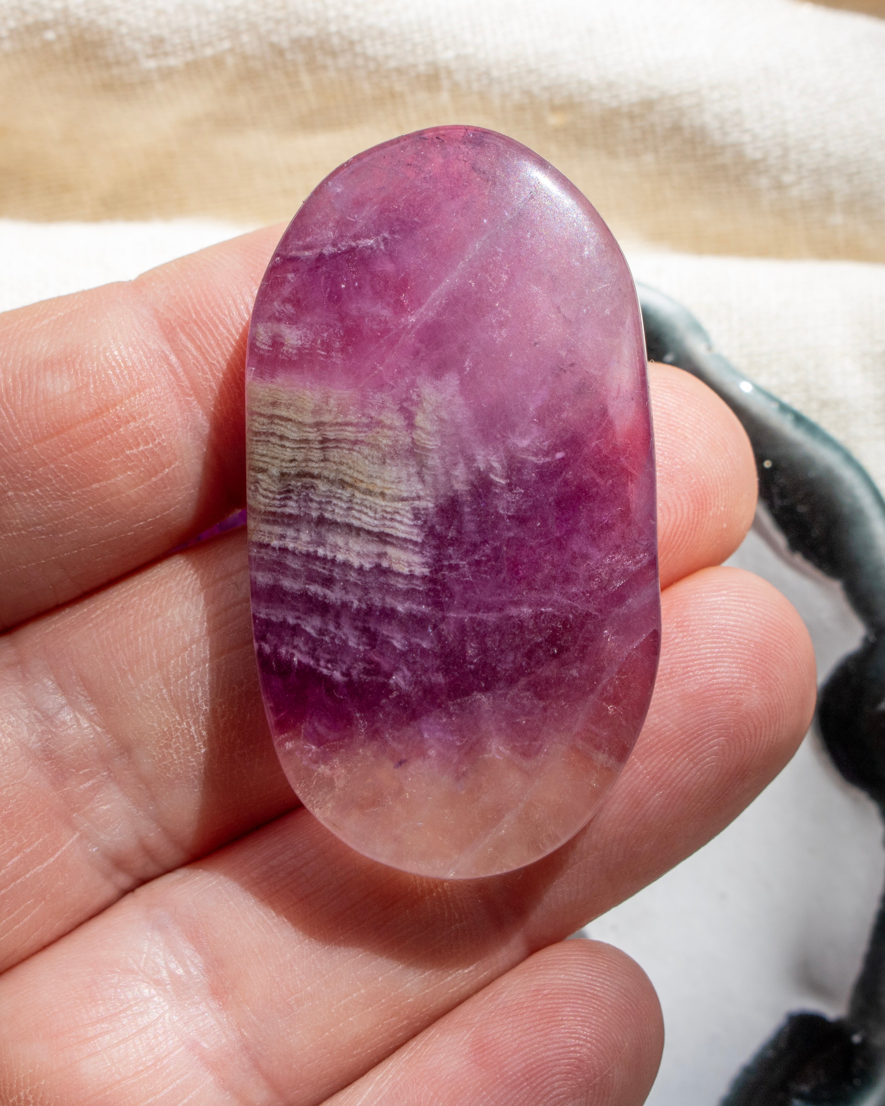 Oval-shaped purple stone held between fingers against a neutral background