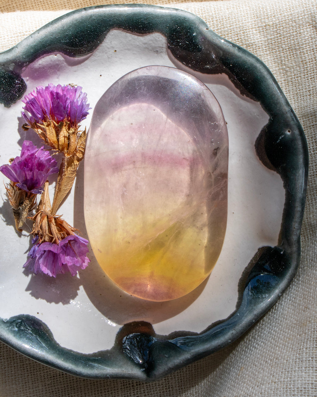 Decorative plate with a colorful stone and purple flowers on a textured fabric background