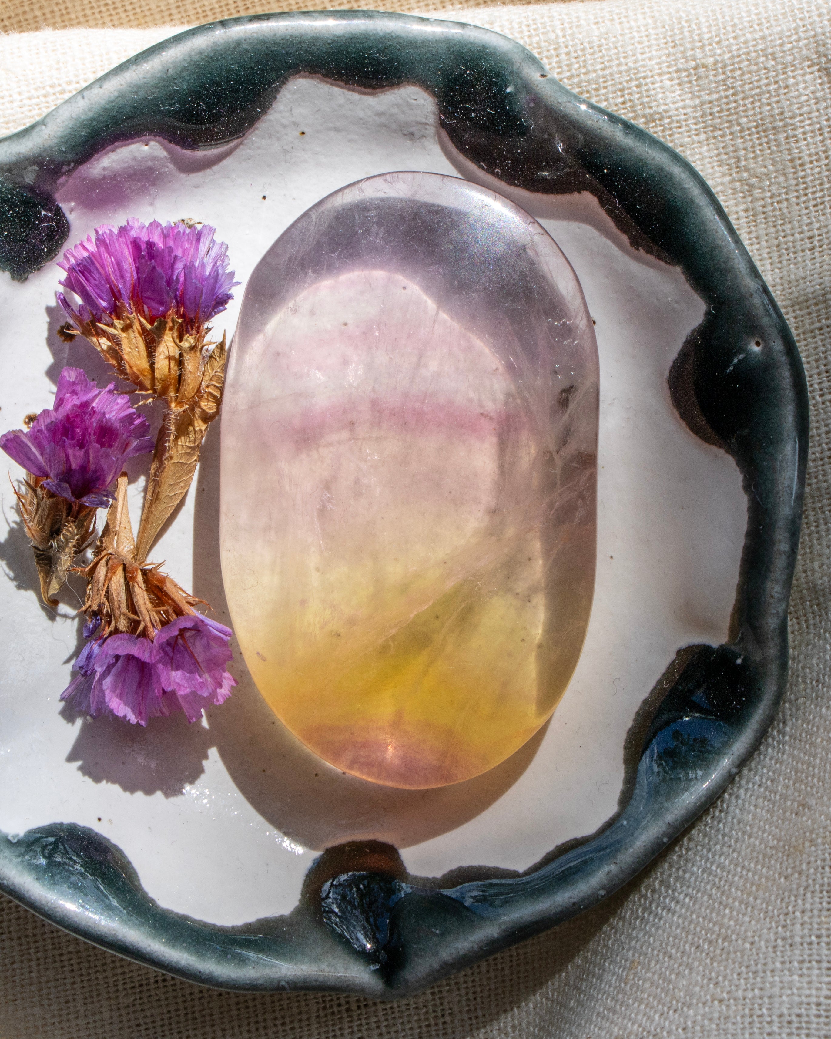 Decorative plate with a colorful stone and purple flowers on a textured fabric background