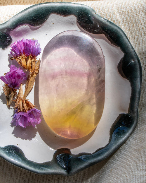 Decorative plate with a colorful stone and purple flowers on a textured fabric background
