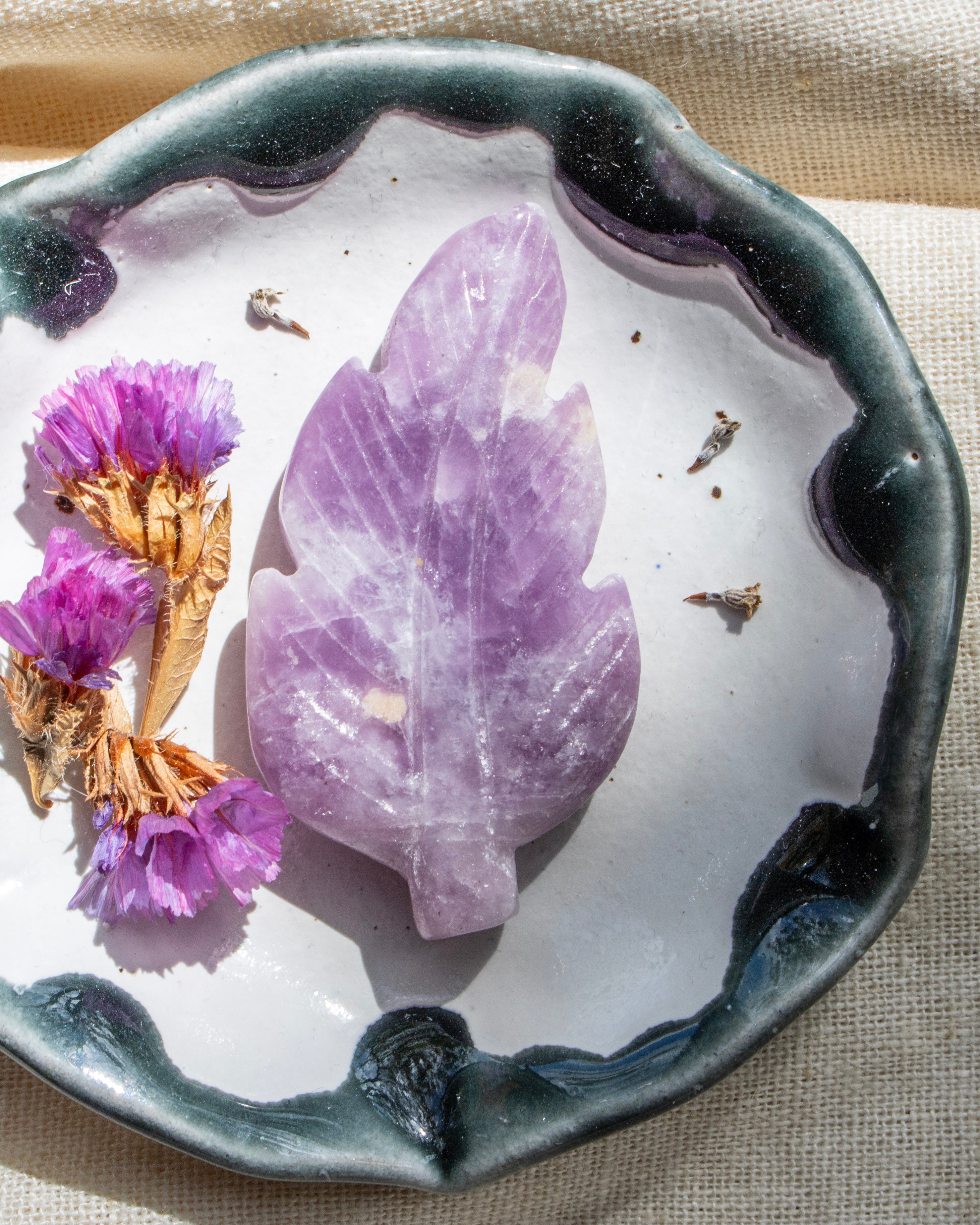 Purple leaf-shaped crystal on a white dish with purple flowers, on a beige fabric background