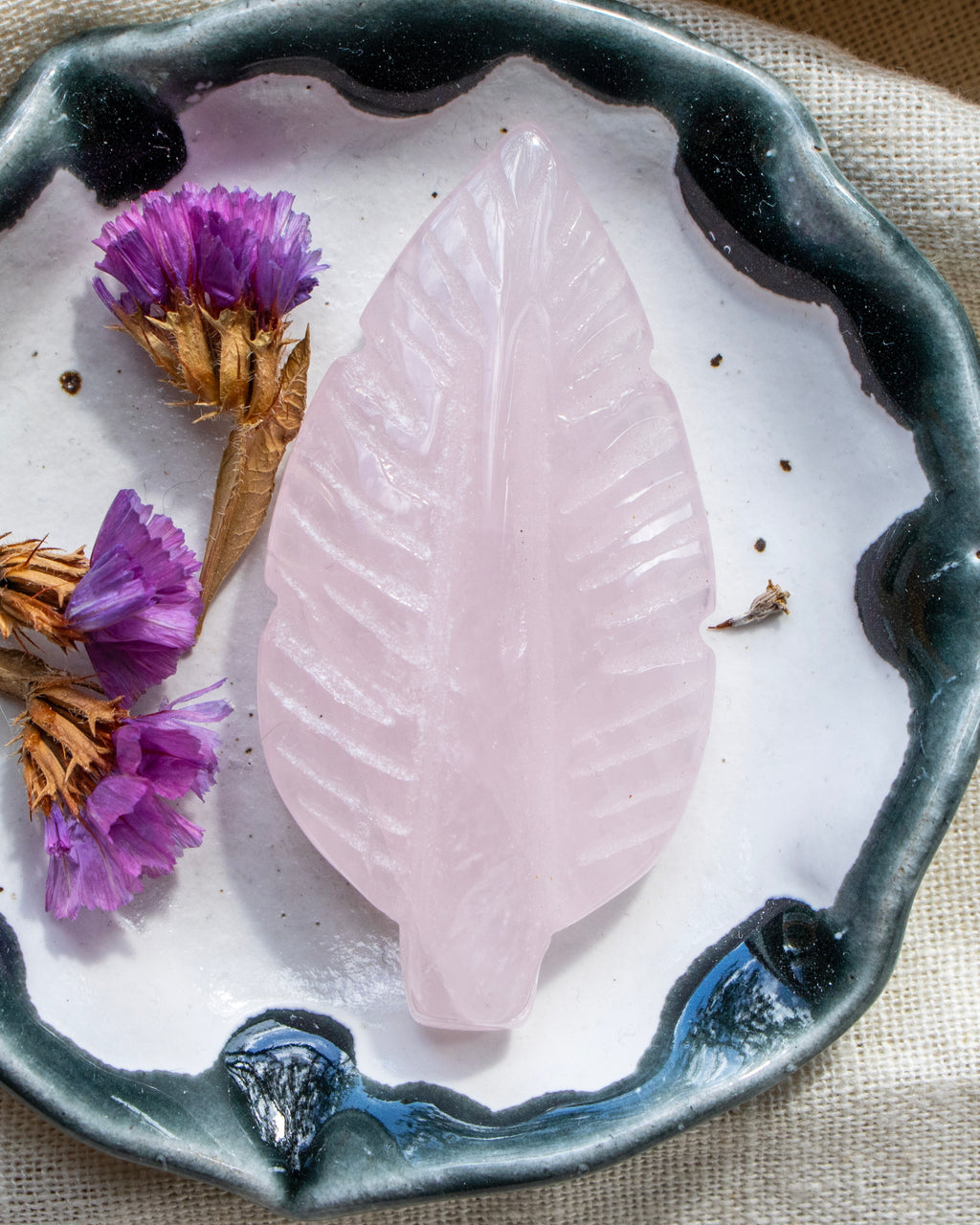 Pink leaf-shaped stone on a white plate with purple flowers and brown leaves.