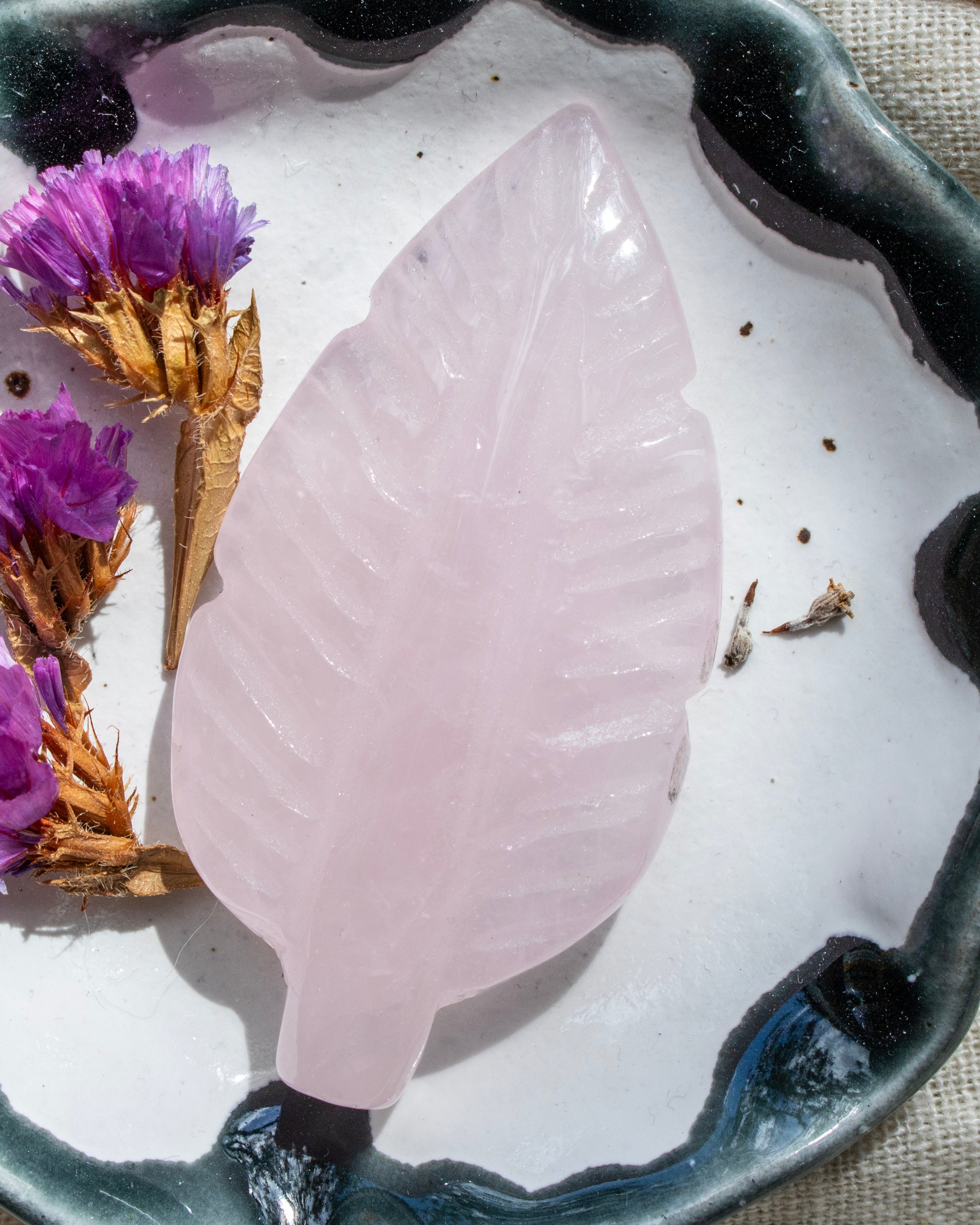 Pink crystal leaf on a white surface with purple flowers and brown leaves.
