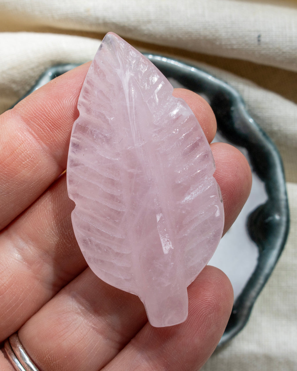 Pink leaf-shaped crystal held in a hand with a blurred background