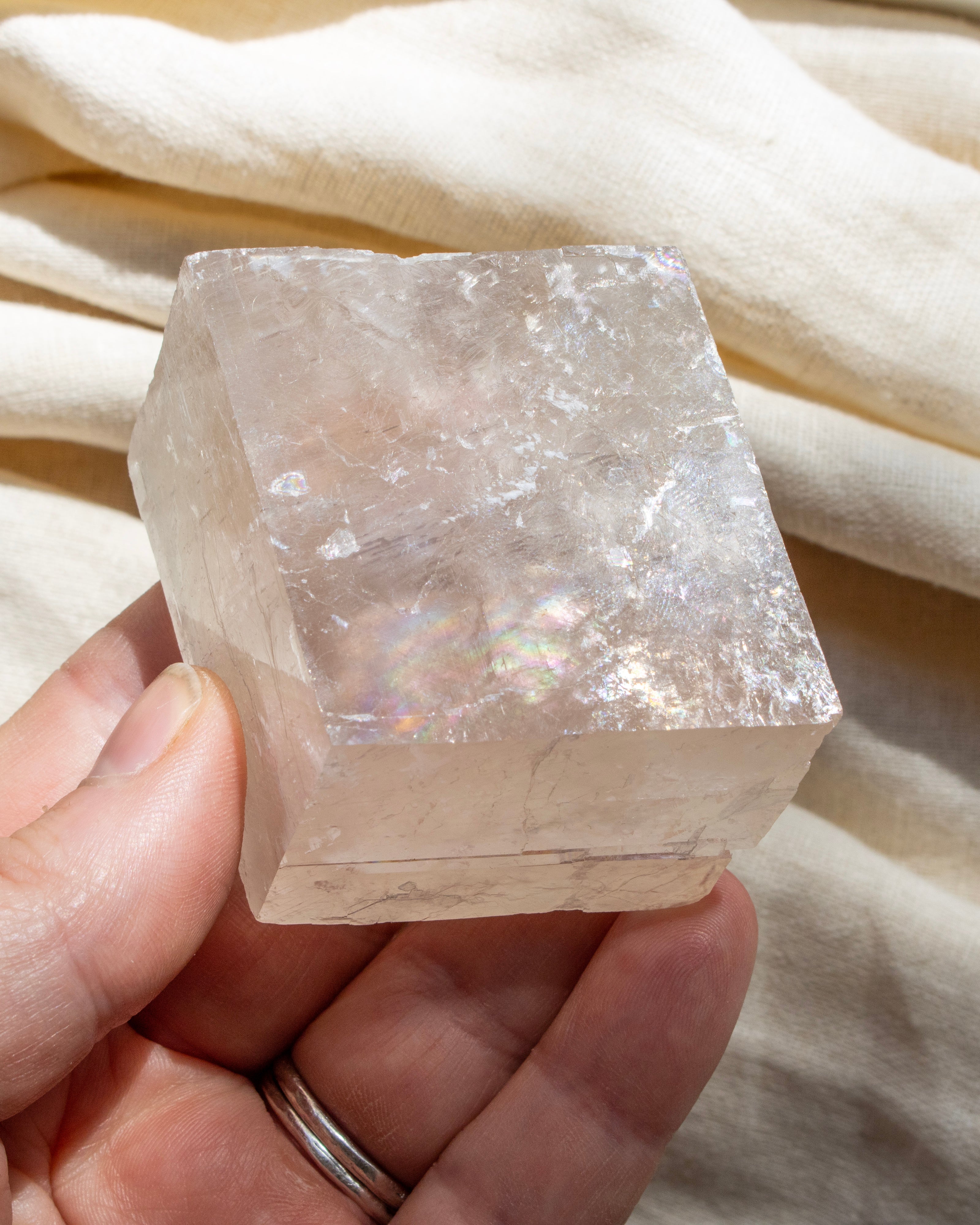 Clear crystal block held in a hand against a beige fabric background